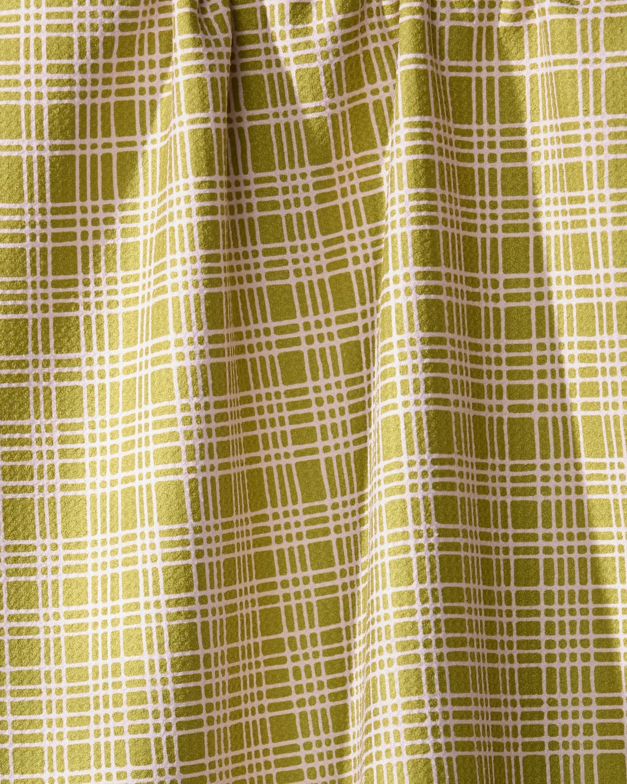 A detailed view of Geometry’s Orchard Plaid Green curtain features a yellow-green grid reminiscent of a tea towel. The eco-friendly fabric is gathered at the top, forming soft vertical folds.