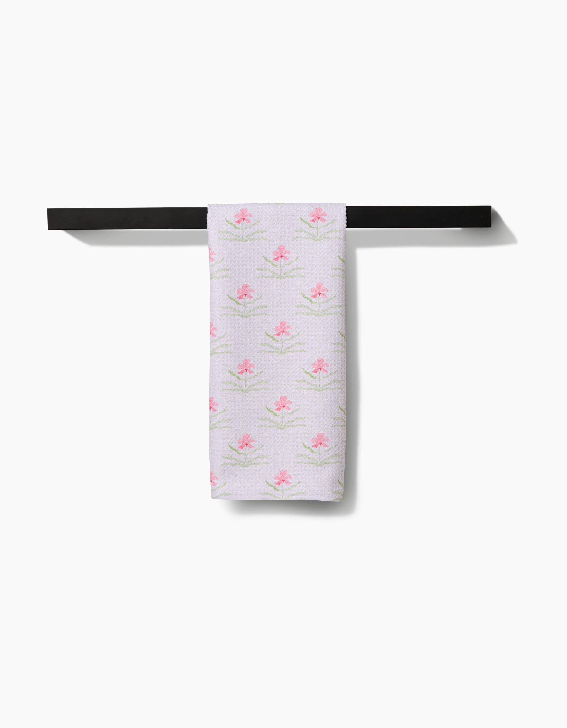The Orchids In Bloom tea towel by Laura Prietto, featuring a pink flower pattern on durable Geoweave fabric, is draped neatly over a black bar against a plain white background.