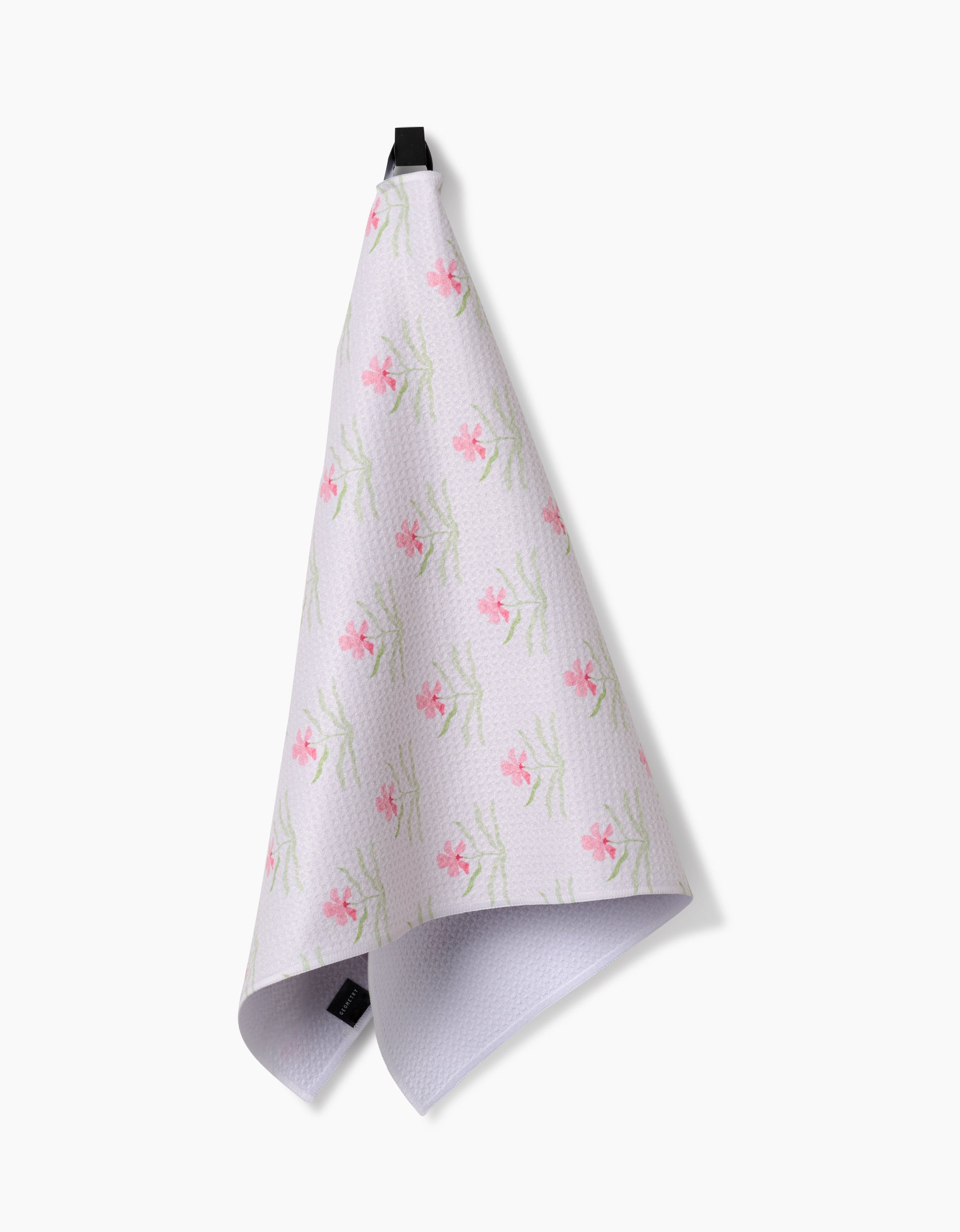 Orchids In Bloom by Laura Prietto—a white Geoweave tea towel with a pink floral pattern—hangs from a black loop against a plain white background.