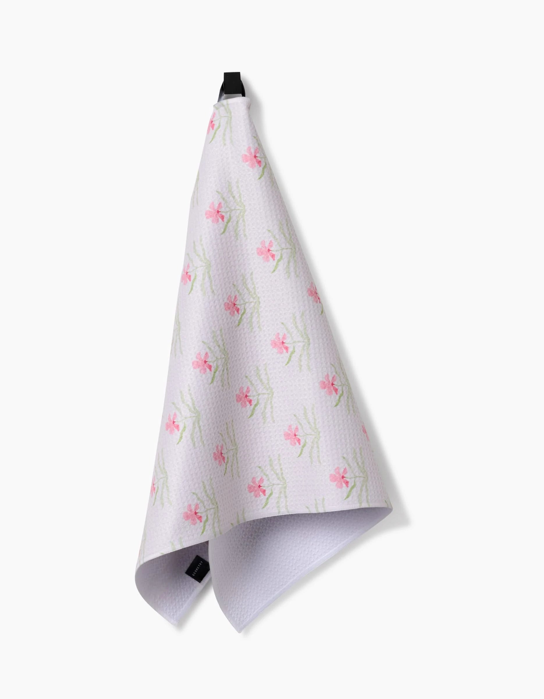 Orchids In Bloom by Laura Prietto—a white Geoweave tea towel with a pink floral pattern—hangs from a black loop against a plain white background.