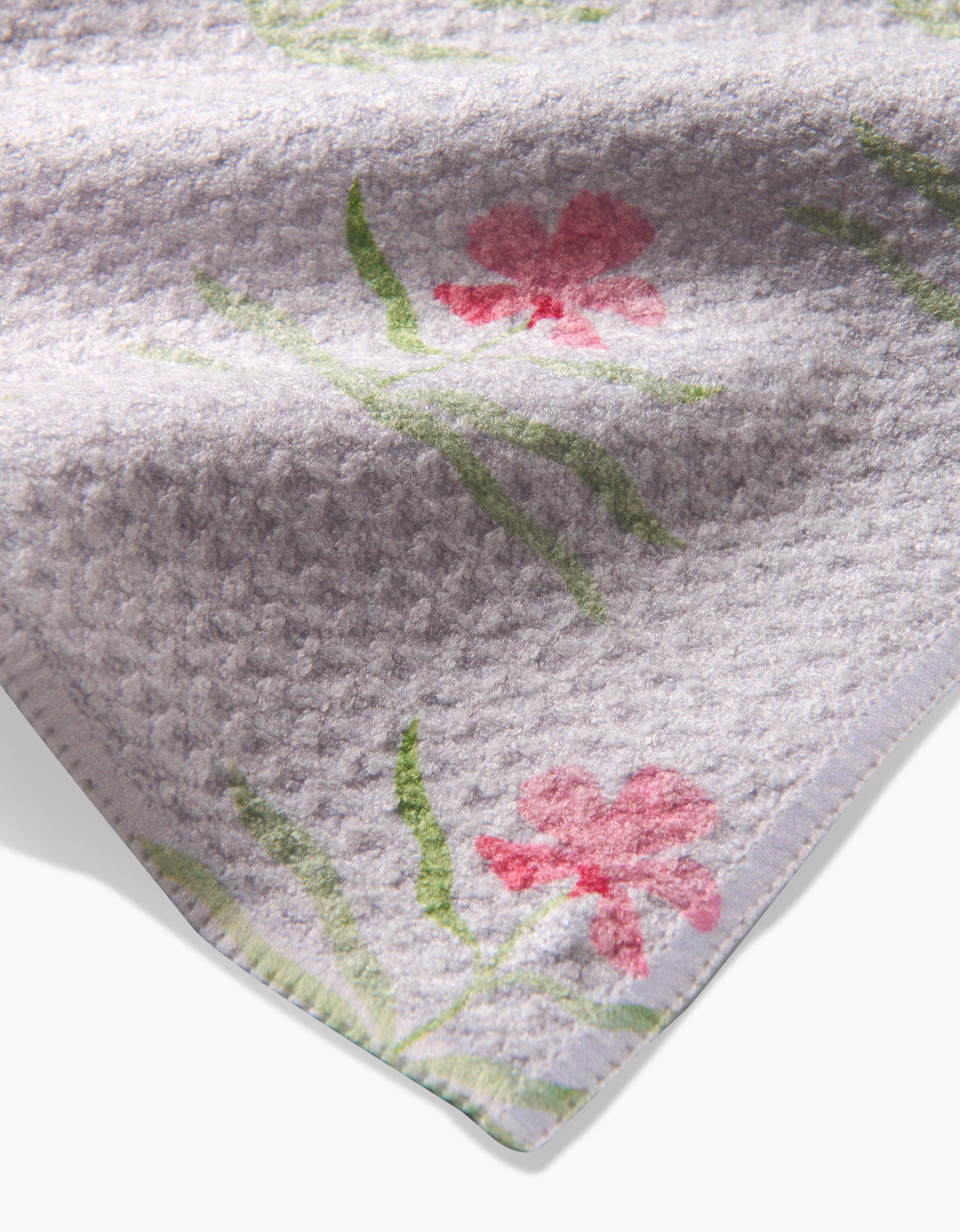 A close-up of the Orchids In Bloom tea towel by Laura Prietto, made from recycled materials, showcases a textured light gray design with subtle pink floral patterns and green stems.