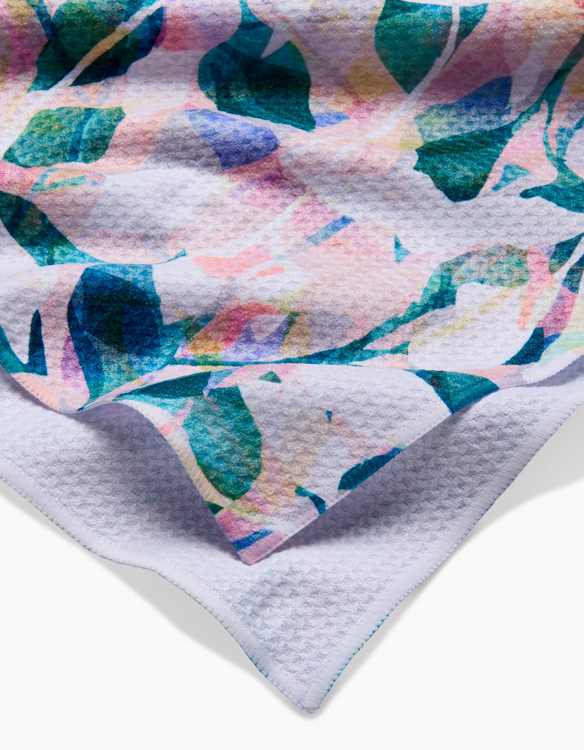 A close-up of the Rachel Parker Painted Foliage tea towel—featuring a soft pastel leafy design in green, blue, pink, and purple—crafted from recycled materials and displayed on a white background with a textured edge.