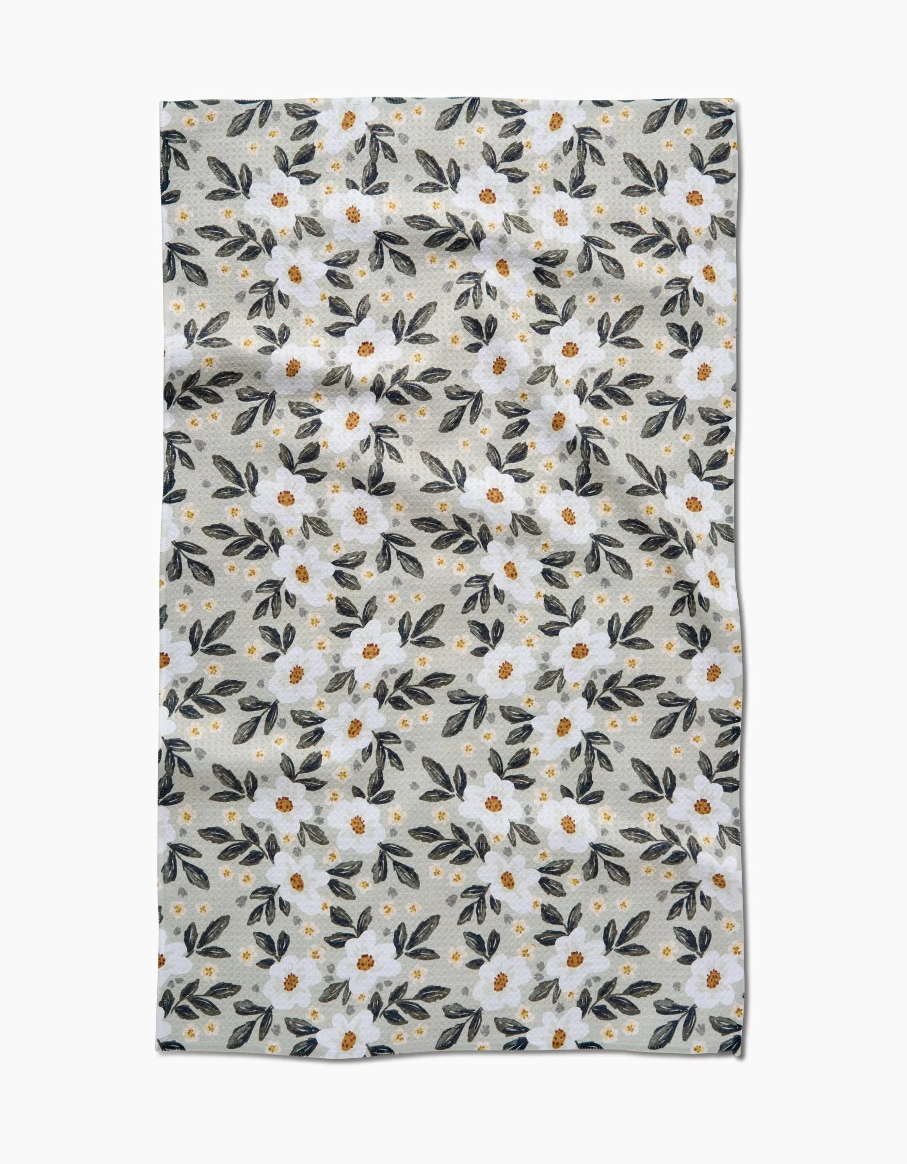 The Painted Spring Flowers Tea Towel by Teri the Butter is made from recycled Geoweave™ fabric. It features white flowers with yellow centers and green leaves on a light beige background, with a naturally wrinkled look.