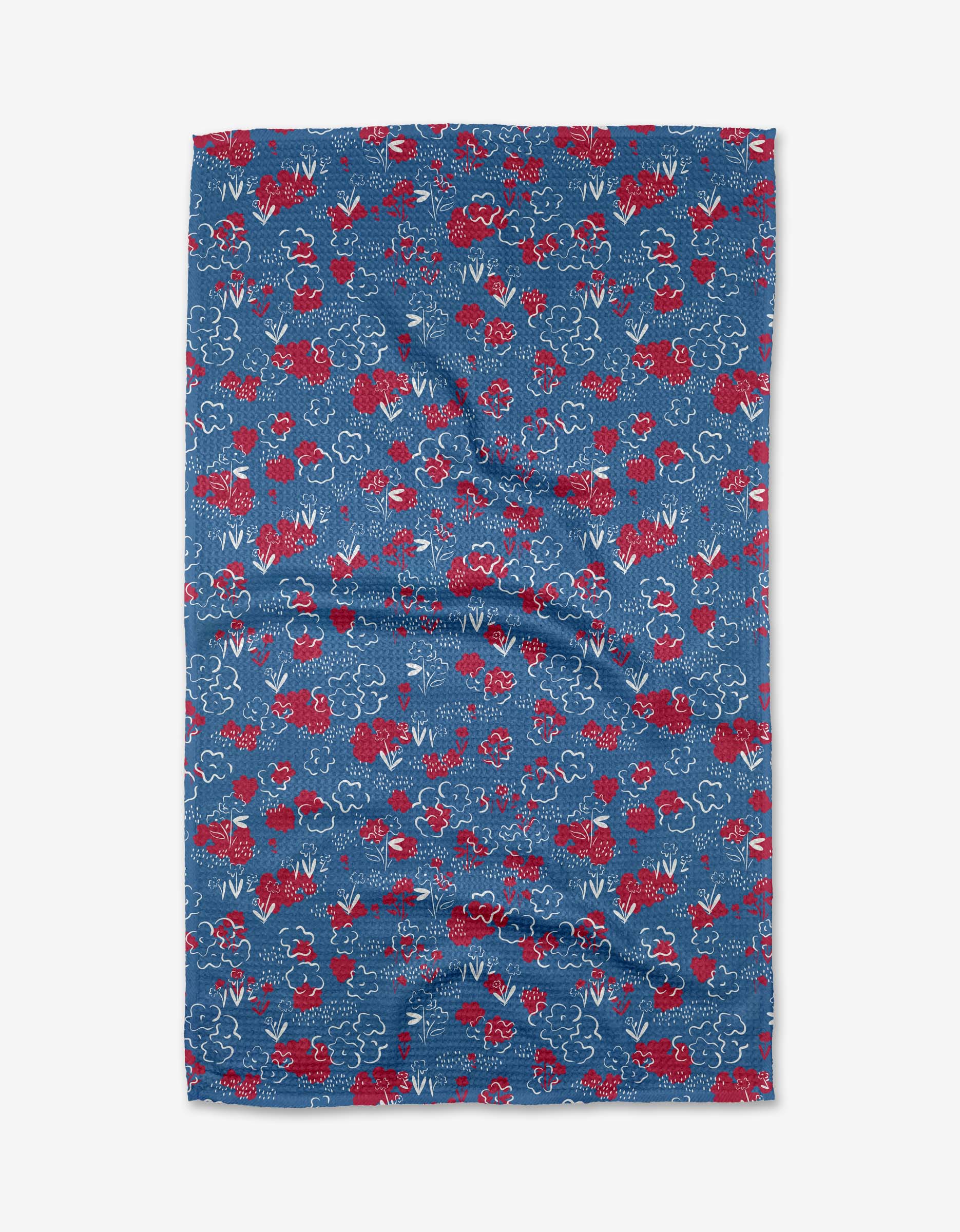 The Patriotic Garden tea towel by Second Nature Studio is rectangular, blue, and textured with red flowers and white cloudlike line designs. Made from quick-drying recycled materials, it’s shown flat on a white background.