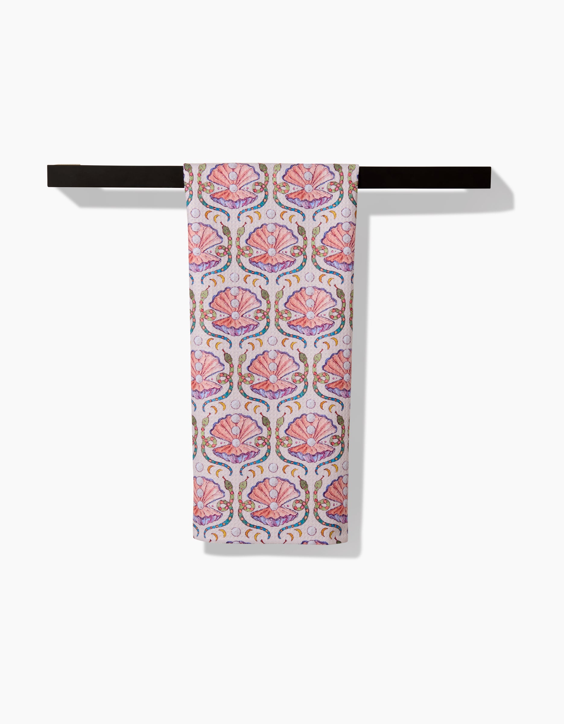 The Pearls Of The Moon towel by Maayan Alper-Swan, showcasing a pink and purple seashell pattern with green and yellow accents, is draped over a black towel bar against a white background.