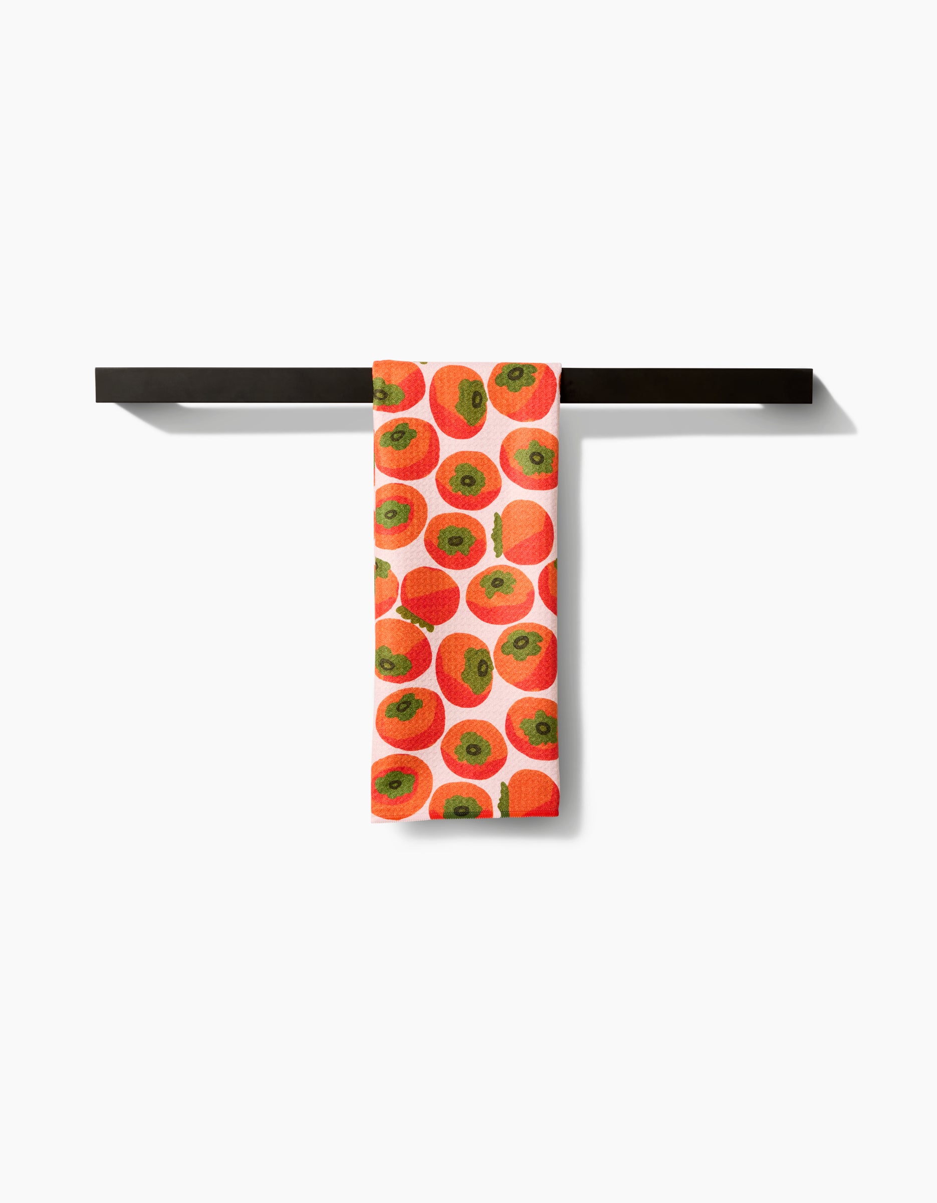 A white Kitchen Tea Towel by Katie OShea featuring a persimmons pattern hangs neatly folded over a horizontal black towel bar, crafted from soft Geoweave fabric against a plain white background.