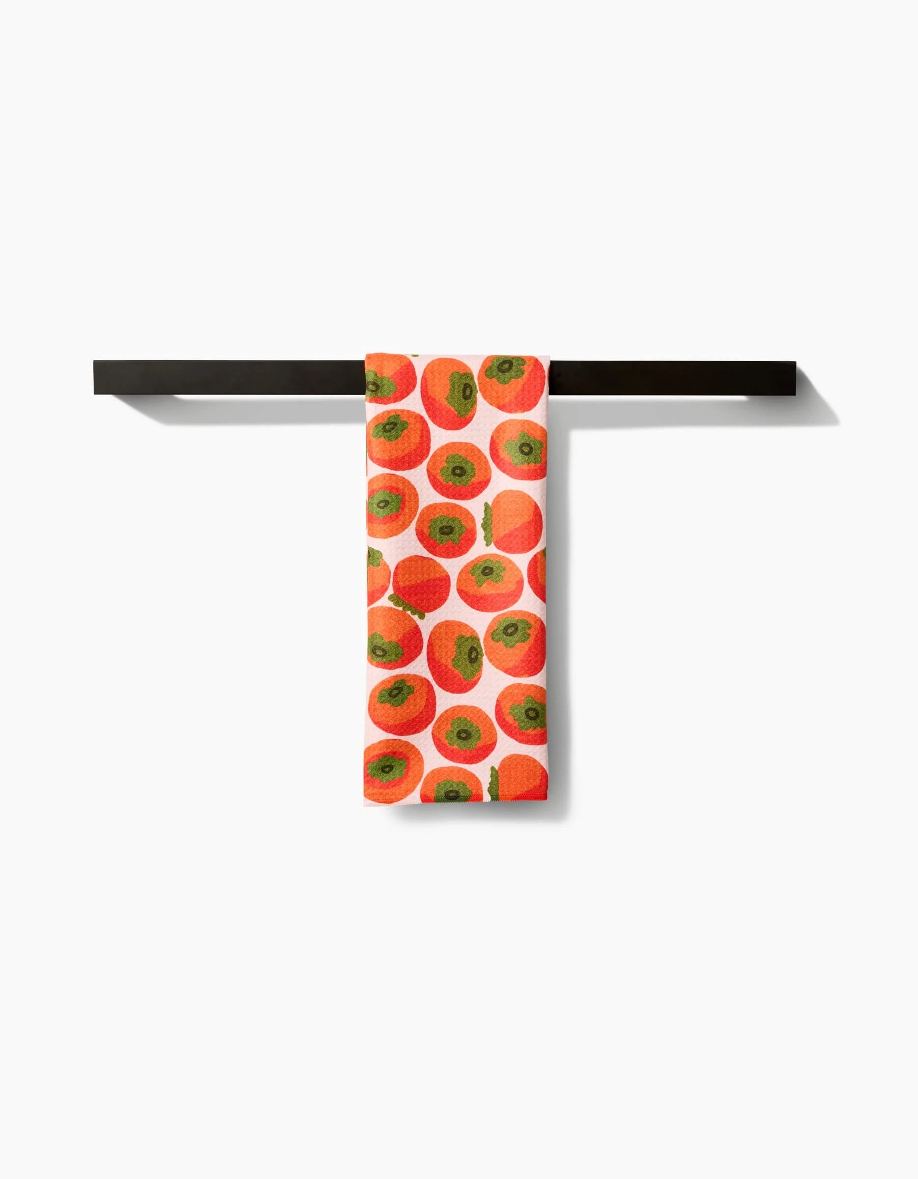 A white Kitchen Tea Towel by Katie OShea featuring a persimmons pattern hangs neatly folded over a horizontal black towel bar, crafted from soft Geoweave fabric against a plain white background.