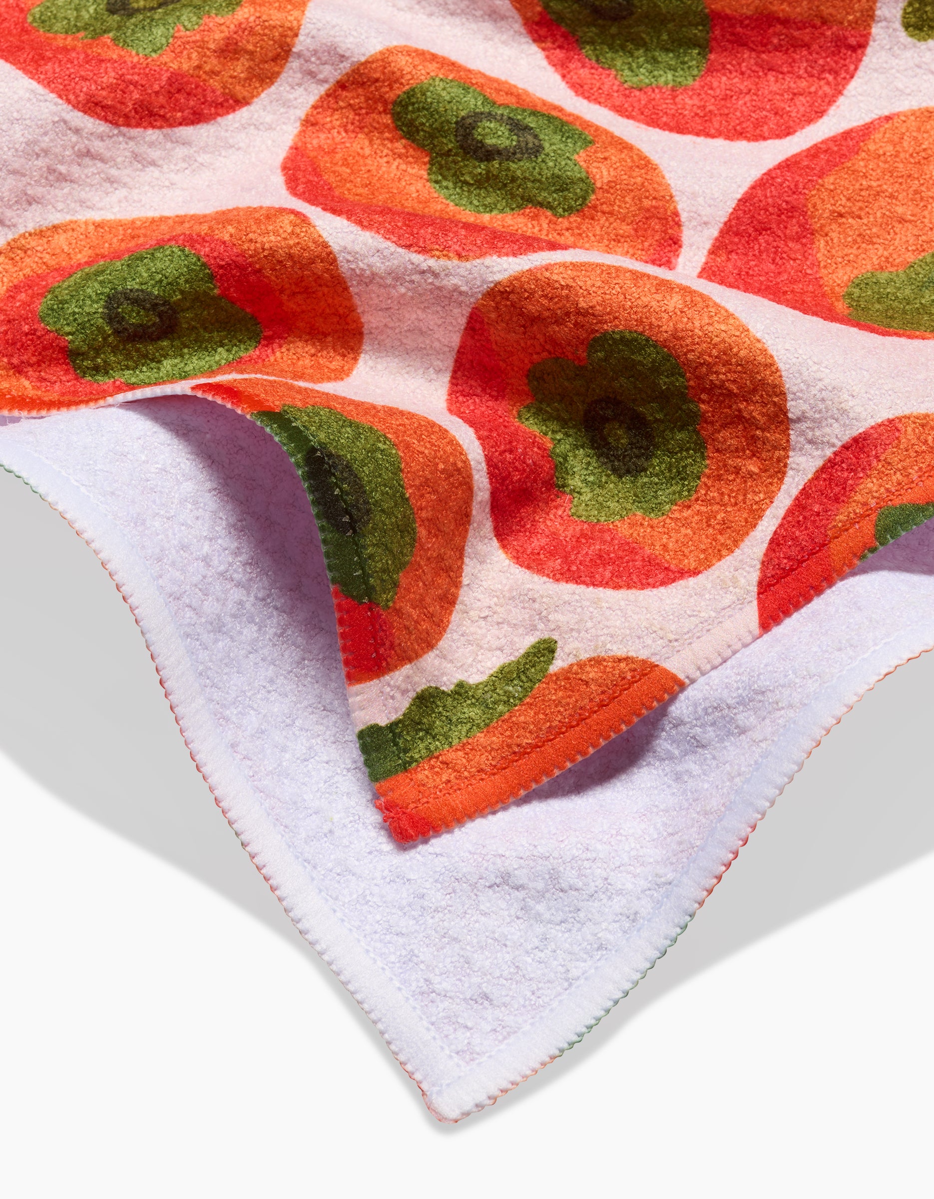A close-up of the Katie OShea Persimmons Kitchen Tea Towel, made from recycled materials and folded to display its vibrant orange and red floral pattern with green centers on white, plus the plain white back.