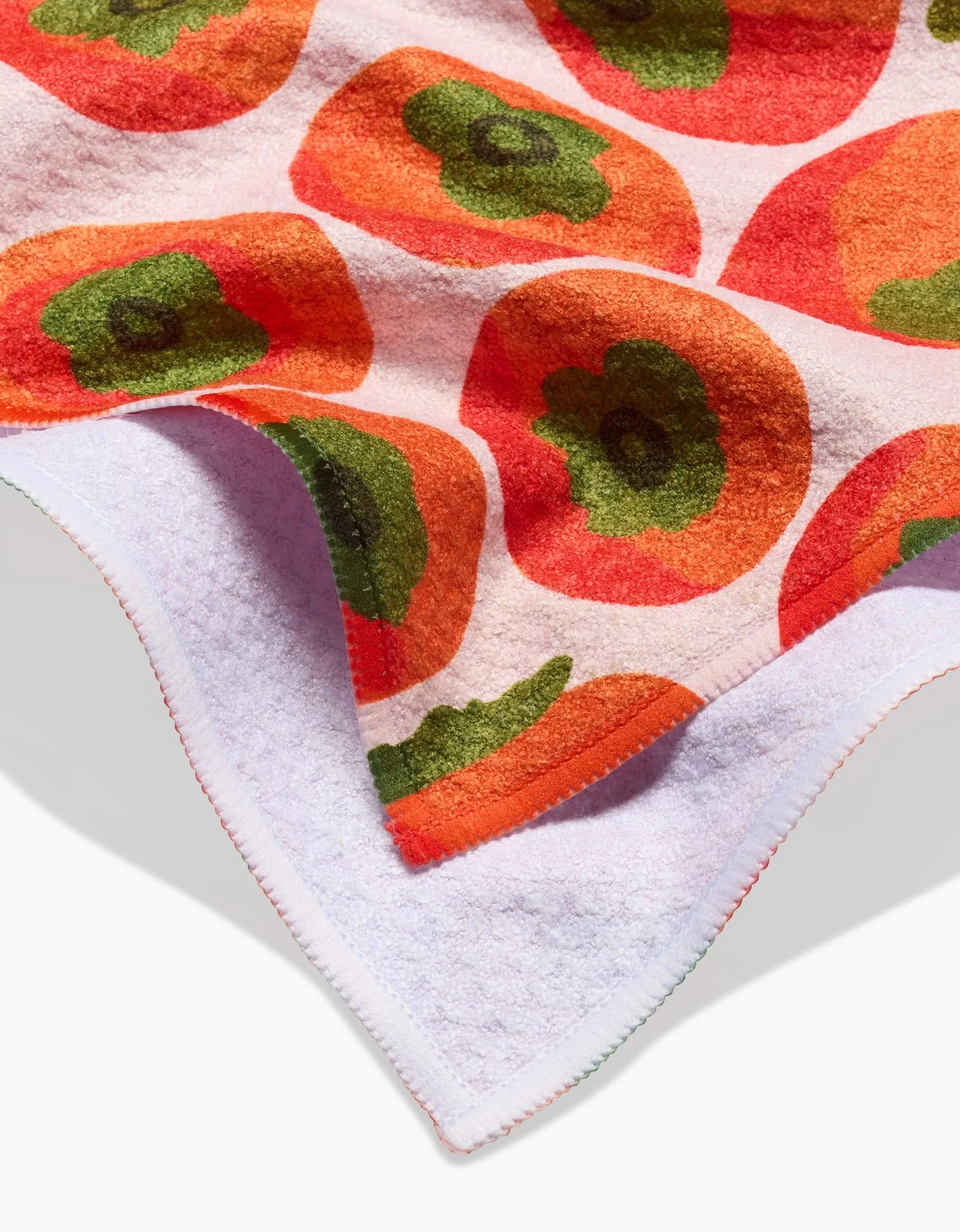 A close-up of the Katie OShea Persimmons Kitchen Tea Towel, made from recycled materials and folded to display its vibrant orange and red floral pattern with green centers on white, plus the plain white back.
