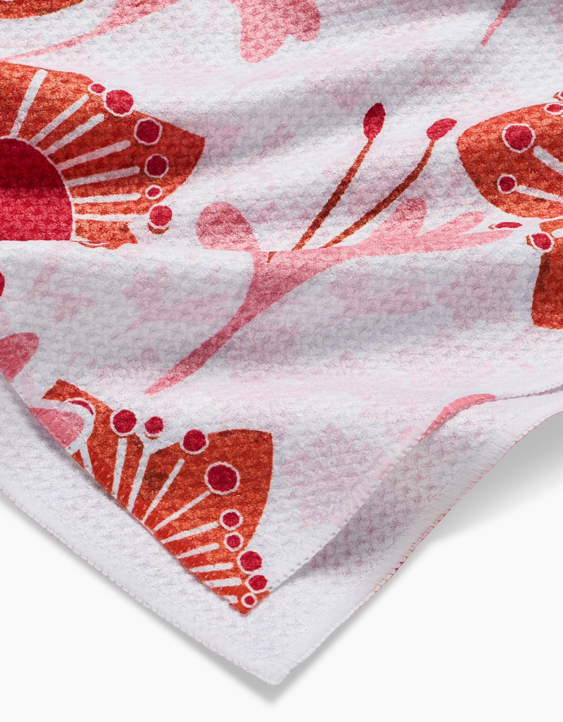 A close-up of Whitney Urquhart’s Petal Paradise tea towel, crafted from recycled materials. It showcases a vibrant red and pink butterfly pattern with abstract floral accents and is slightly folded at the corner.
