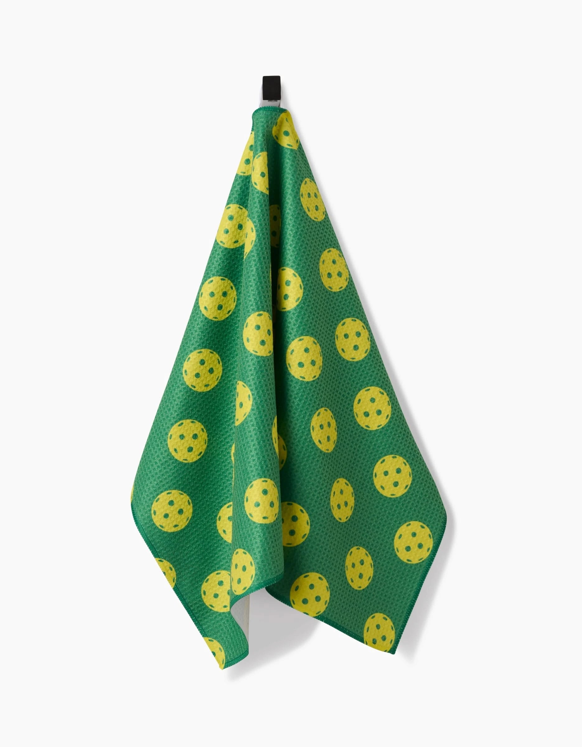 A GEOMETRY Pickleball tea towel with yellow polka dots and blue speckles hangs from a black hook against a white background.