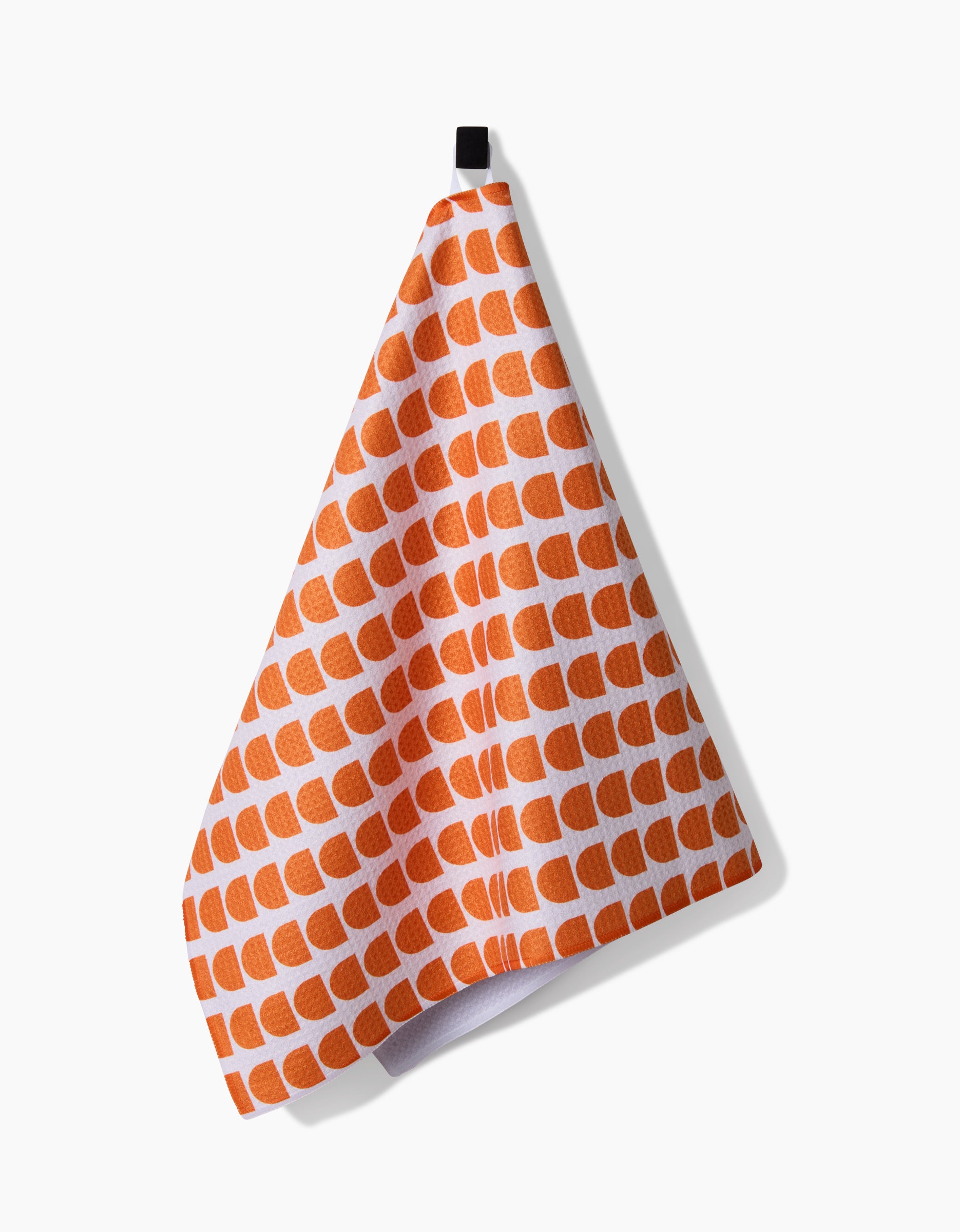 A Pink Illusion towel by Happy Hemera, featuring an orange semicircle pattern on white ultra-absorbent Geoweave™ fabric, hangs from a black loop against a plain white background.
