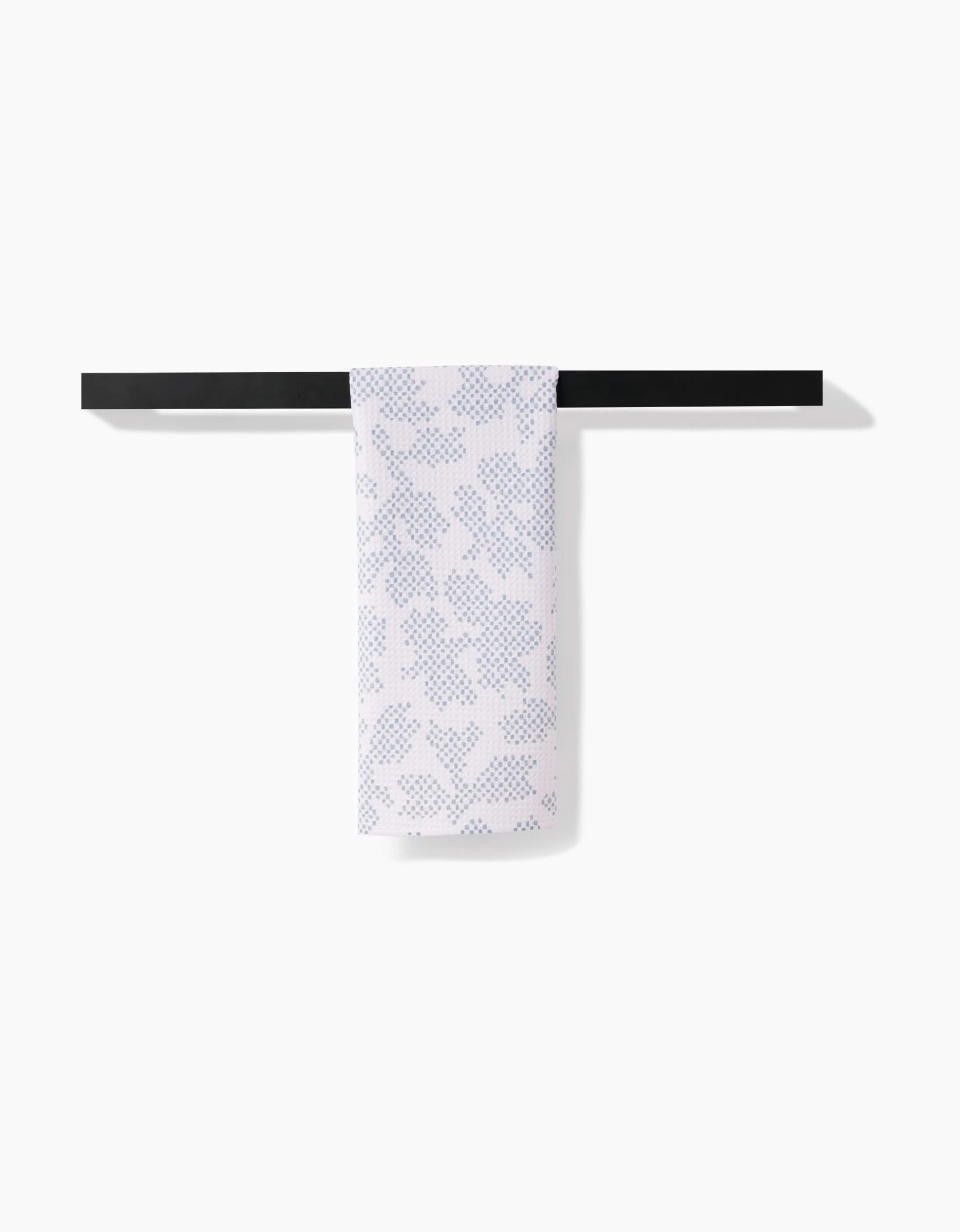 The Pixie Sage tea towel by Studio Jeannot, crafted from soft Geoweave™ fabric, features a blue dotted leaf and heart pattern and is shown draped on a black towel bar against a white background.