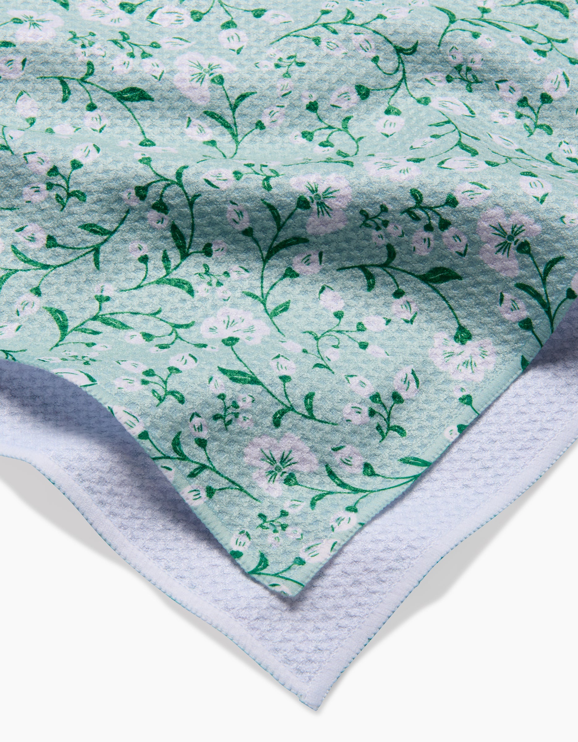 A close-up of the light blue Geoweave fabric from Danelys Sidron’s Plumbago Bloom tea towel, featuring a green and white floral pattern layered over textured white fabric.