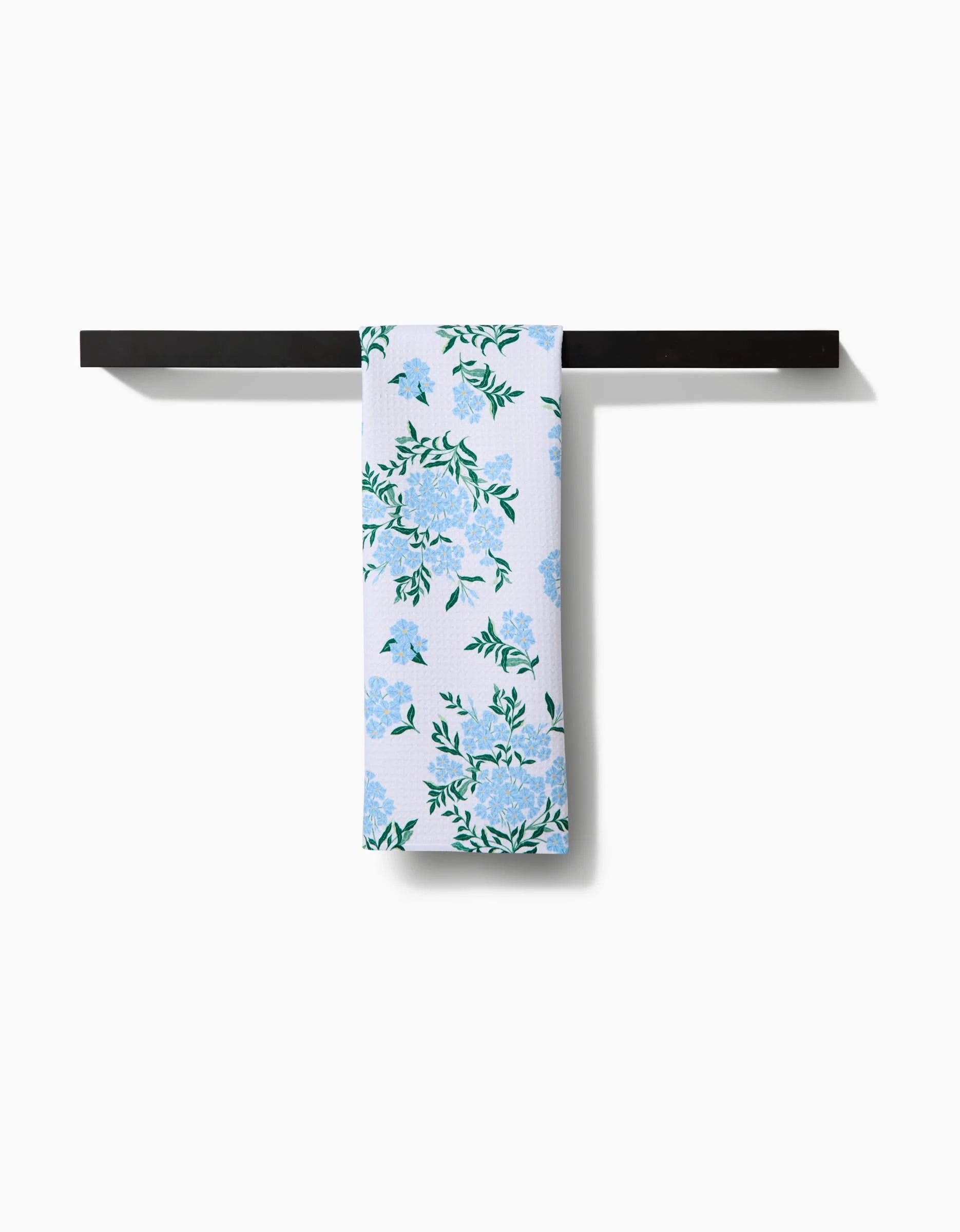 The Danelys Sidron Plumbago towel, featuring blue and green floral patterns on ultra-absorbent Geoweave™ fabric, is draped over a black horizontal bar against a plain white background.