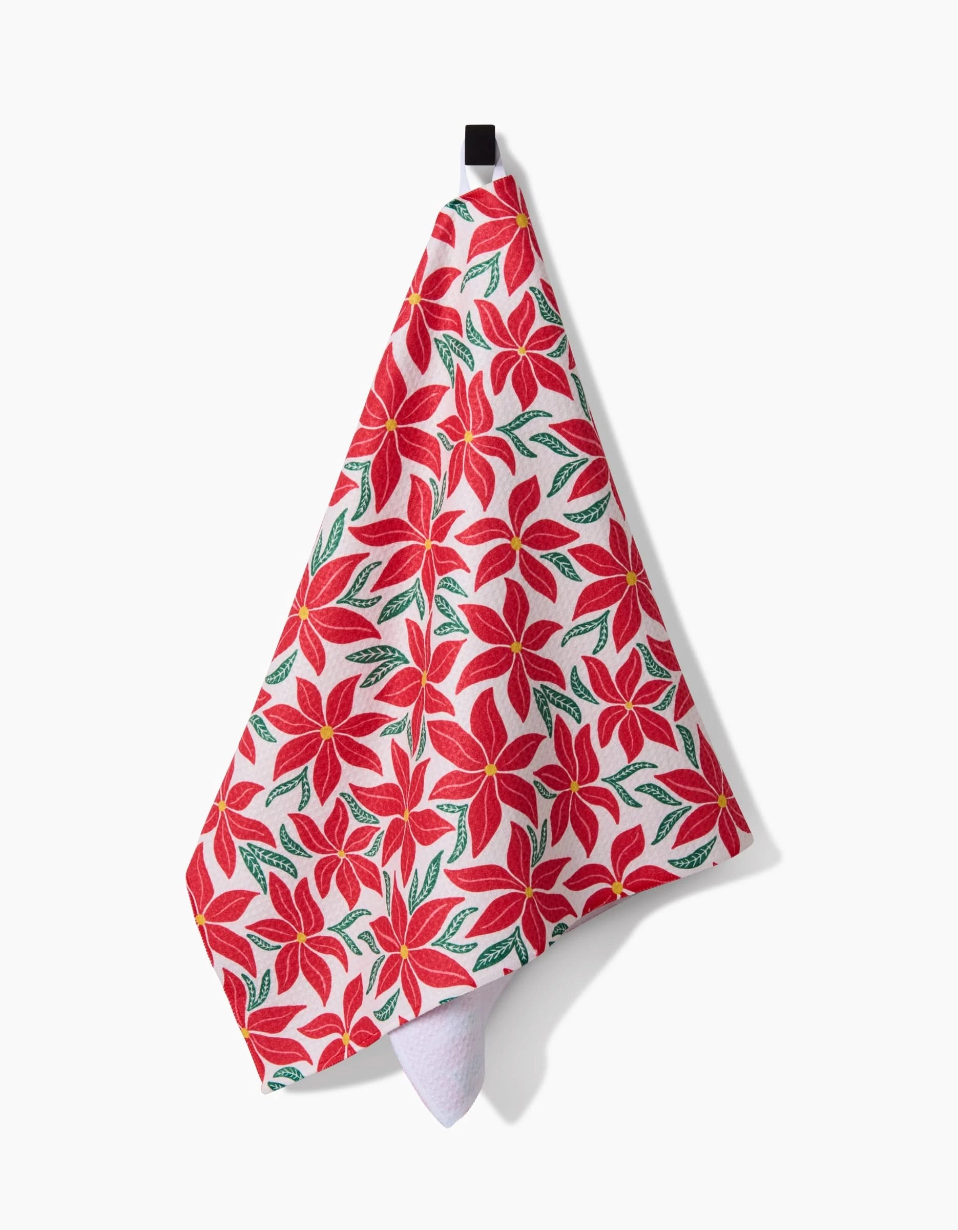 The Kayla Ann Poinsettia Party tea towel, made from recycled materials, features a vibrant red poinsettia and green leaf pattern and hangs from a black loop against a white background.