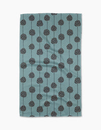 The Polka Dot Garland tea towel by Lizzie Clark is made from recycled materials in teal, with a pattern of black round flowers with white dots and thin stems arranged in vertical rows. The slightly wrinkled fabric is displayed on a white background.