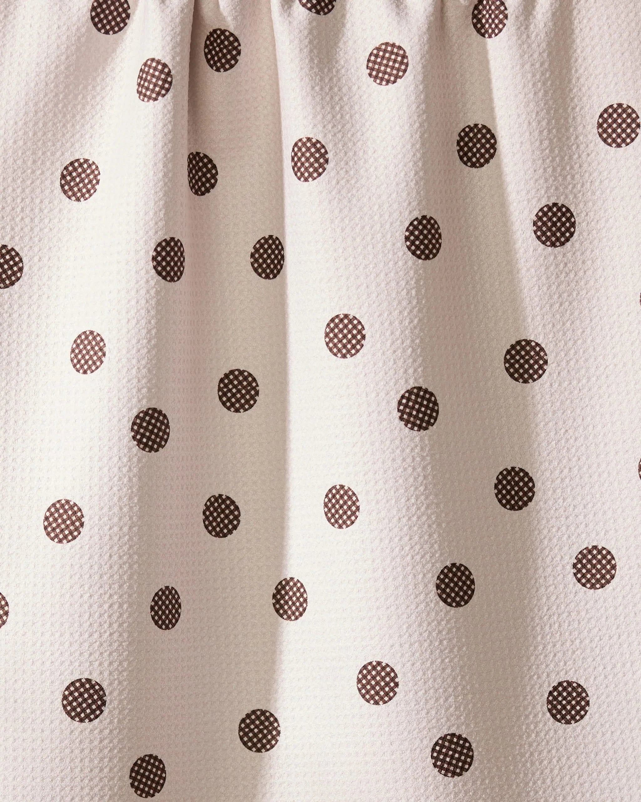Close-up of Geometry’s Polka Picnic recycled kitchen towel, featuring small brown polka dots on white fabric. The top is gathered, creating soft folds and a textured look.