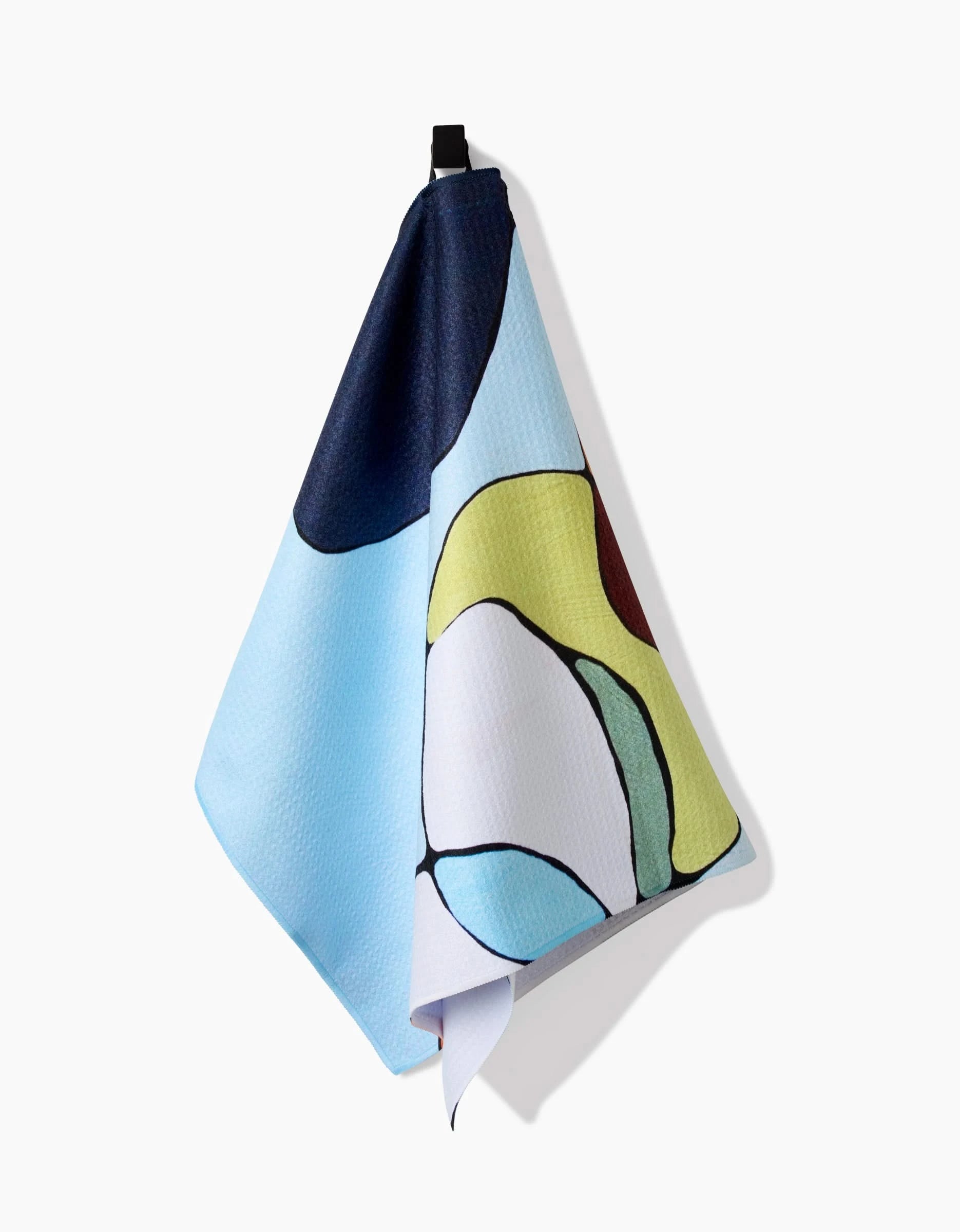 The Poppies on Blue Tea Towel by Rachel Austin, crafted from Geoweave fabric with blue, yellow, black, and white abstract shapes, hangs from a black hook against a plain white background.