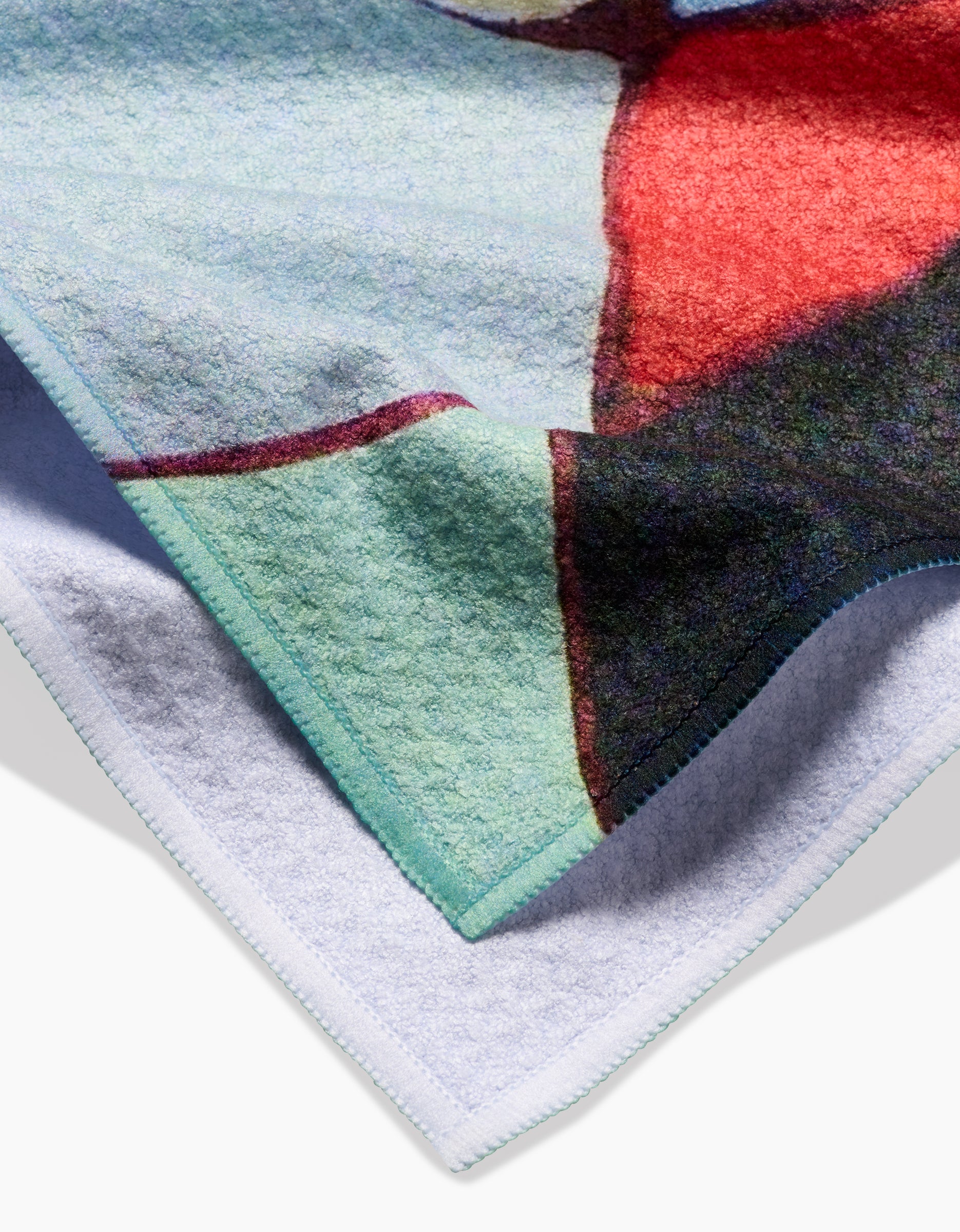 A close-up of the Rachel Austin Poppies on Mint blanket, made from recycled materials, featuring abstract red, green, and black patterns on one side and plain white on the reverse with neatly stitched edges.