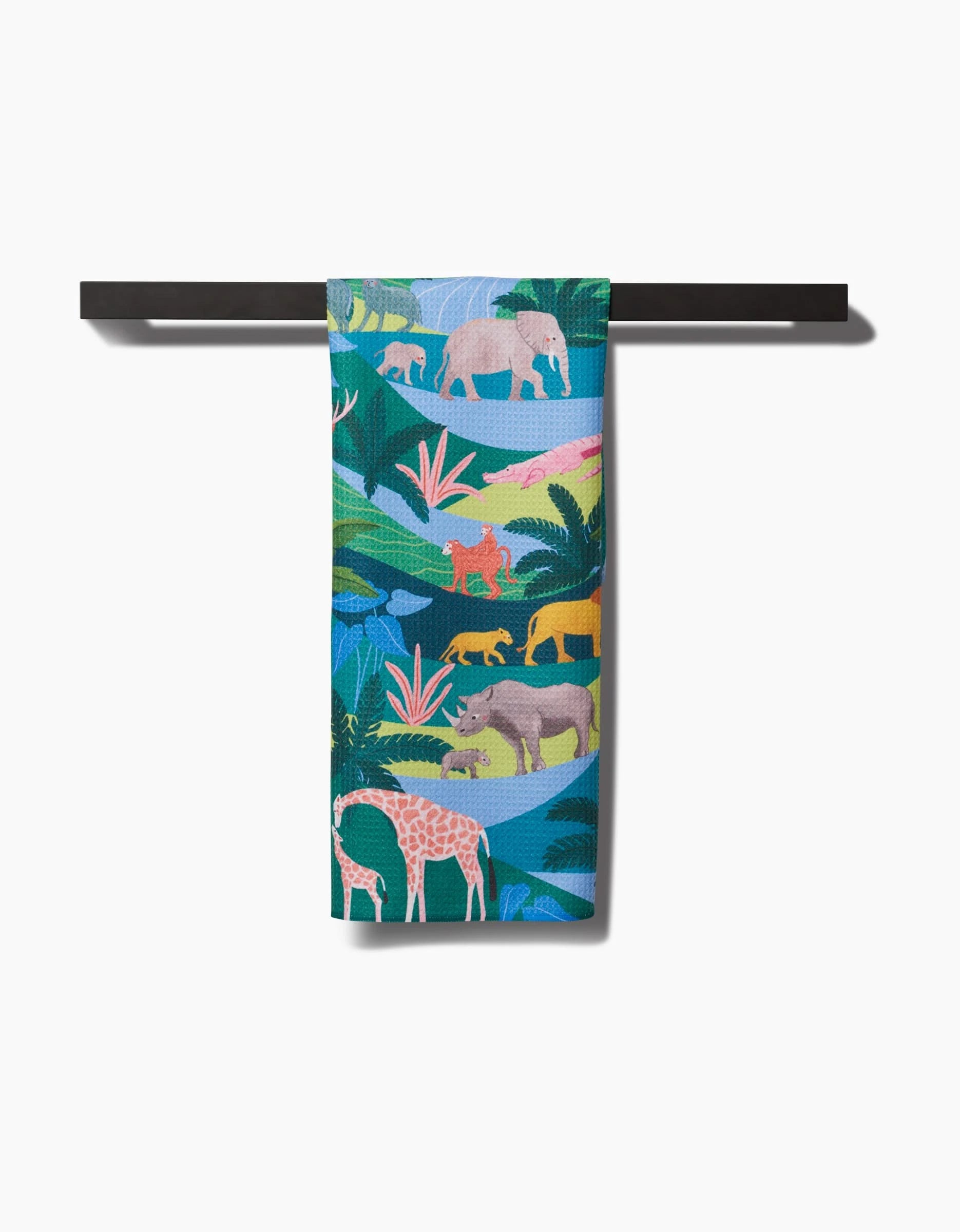 The Rain Forest Tea Towel by Ceyda Alasar, made from post-consumer recycled materials, displays vibrant illustrations of jungle animals—elephants, lions, giraffes, and birds—hanging on a black bar against a white background.