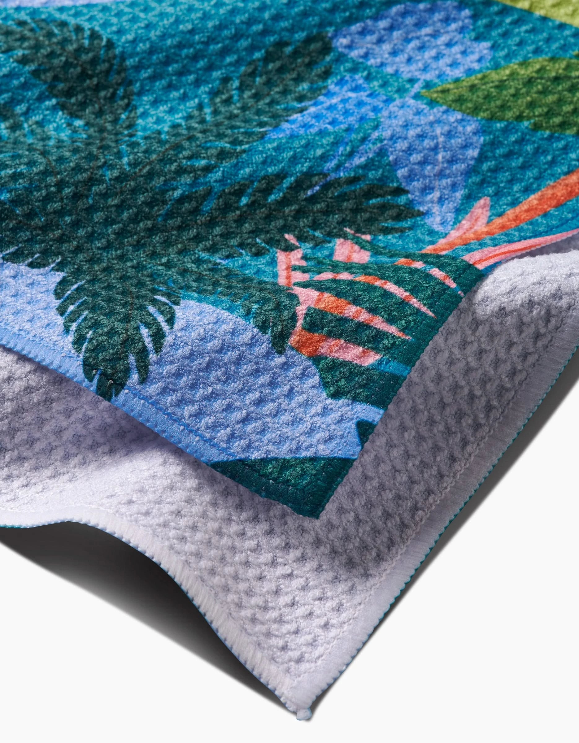 A close-up of Ceyda Alasar’s Rain Forest Tea Towel, showcasing a vibrant tropical leaf design on one side and white, waffle-textured Geoweave™ fabric made from post-consumer recycled materials on the reverse.