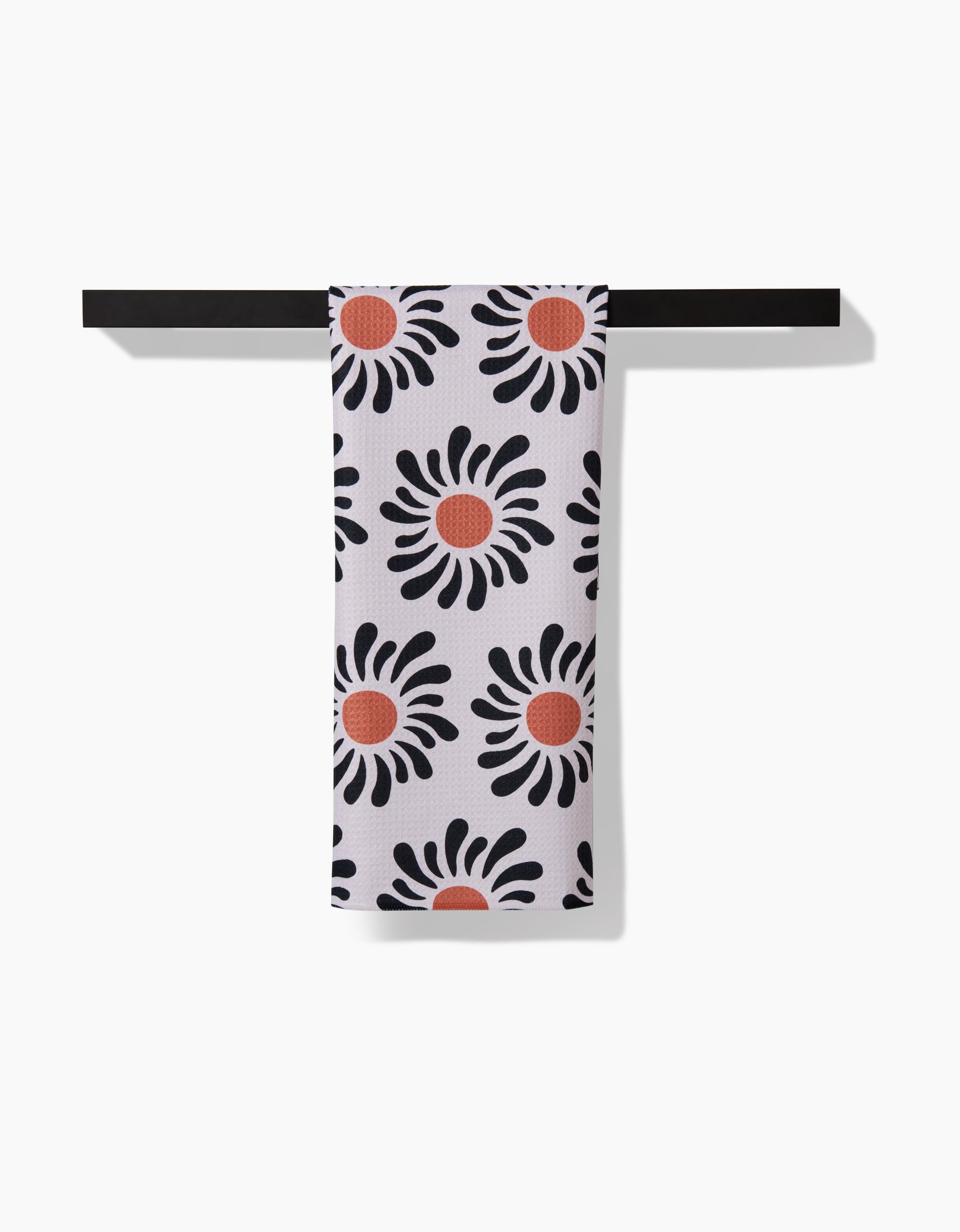 The Realm Refillery eco-friendly white tea towel, featuring a black petal and red center floral design, hangs neatly on a black bar against a white background.