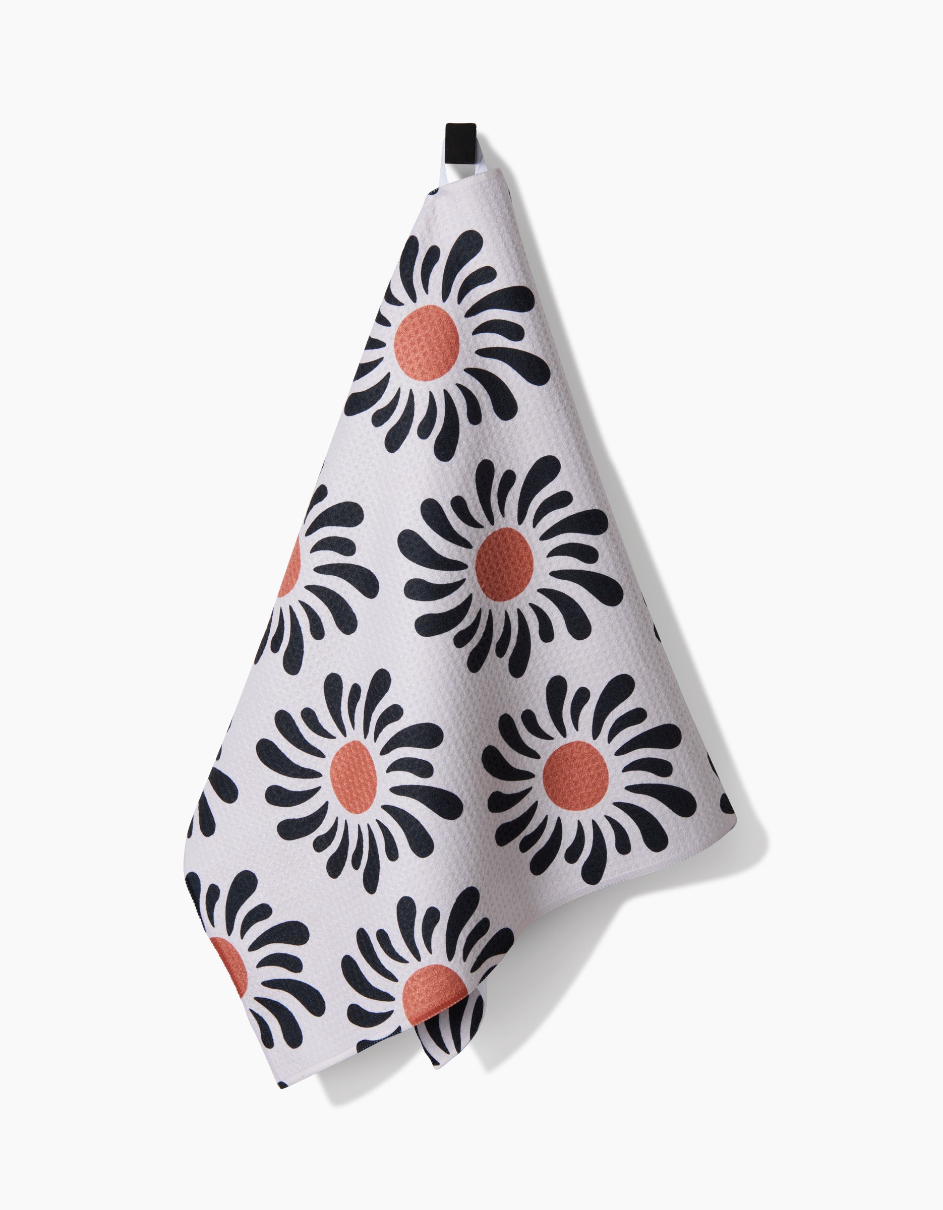 A Realm Refillery tea towel by Realm Refillery, crafted from eco-friendly Geoweave fabric, displays black petal shapes with orange-red centers and hangs by a black loop against a white background.