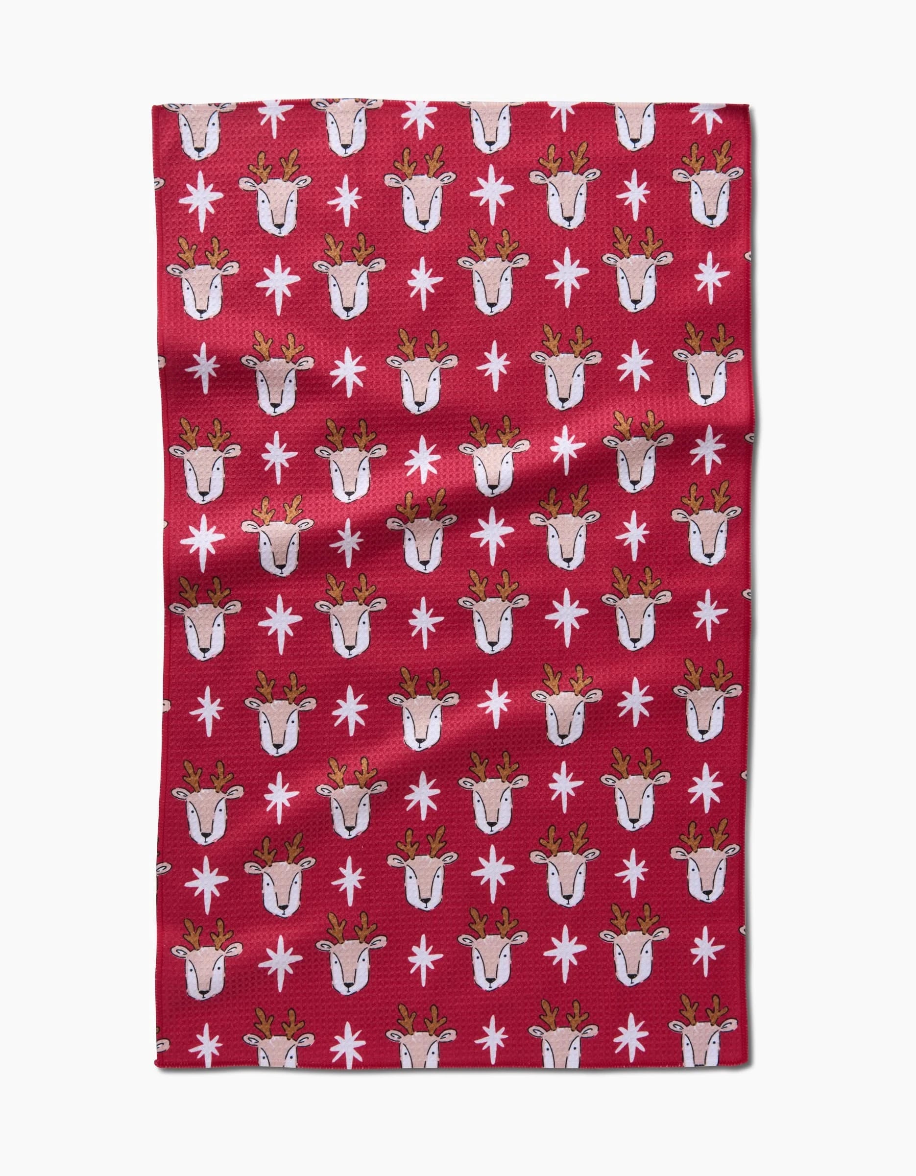 The Reindeer Star tea towel by Hufton Studio is a quick-drying, eco-friendly red towel with rows of cartoon reindeer faces and white snowflakes, made from recycled materials.
