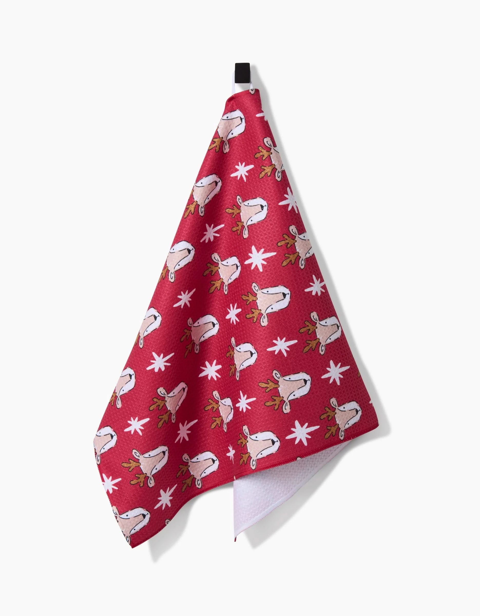 The Reindeer Star kitchen towel by Hufton Studio features cartoon reindeer faces and white snowflakes in red, made from recycled materials, and hangs by a black loop against a white background.
