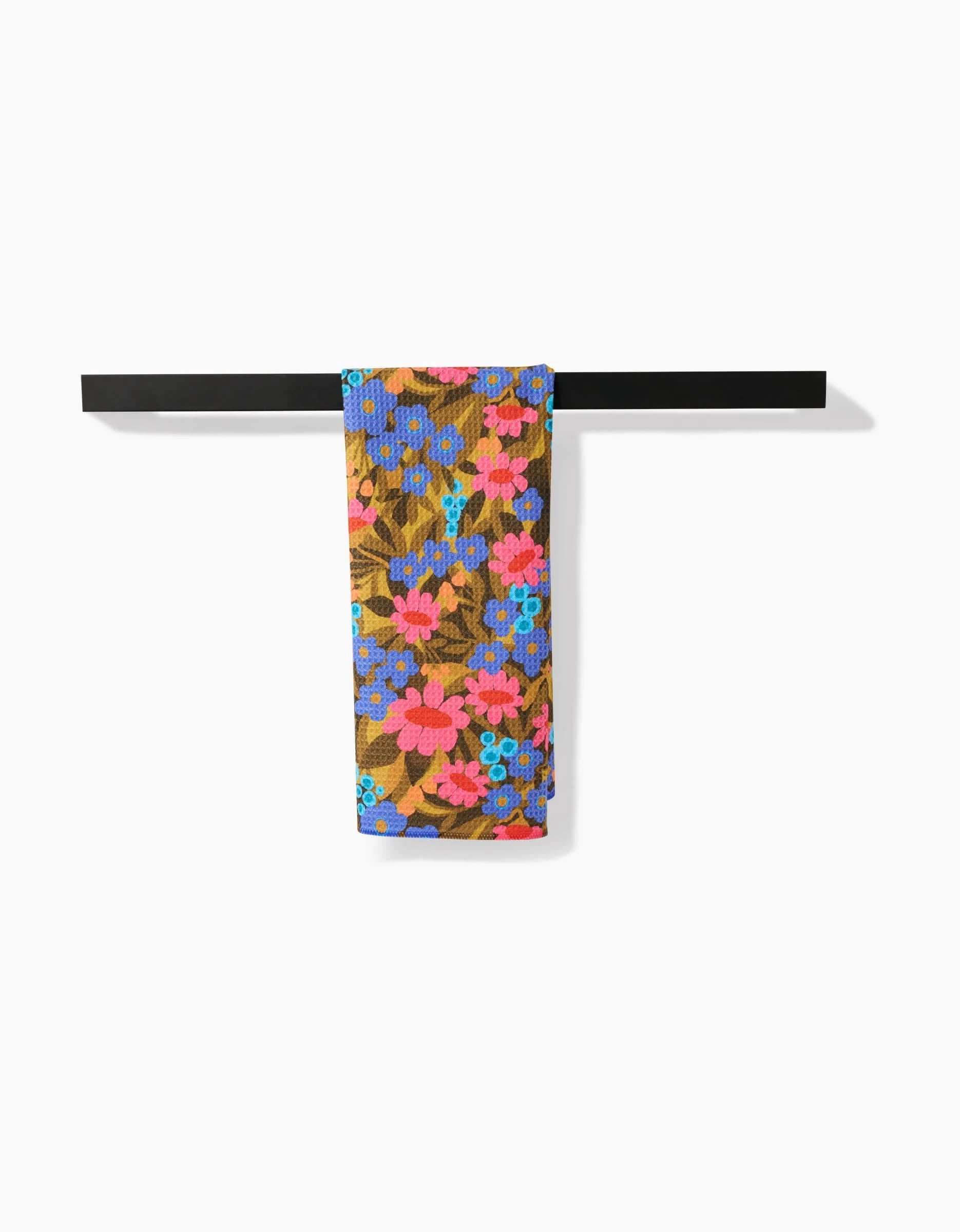 A vibrant Retro Garden tea towel by Lisa Nelson, featuring a floral pattern in pink, blue, and red, hangs on a black rack. Crafted from ultra-absorbent Geoweave fabric, it brings both style and function to the white background.