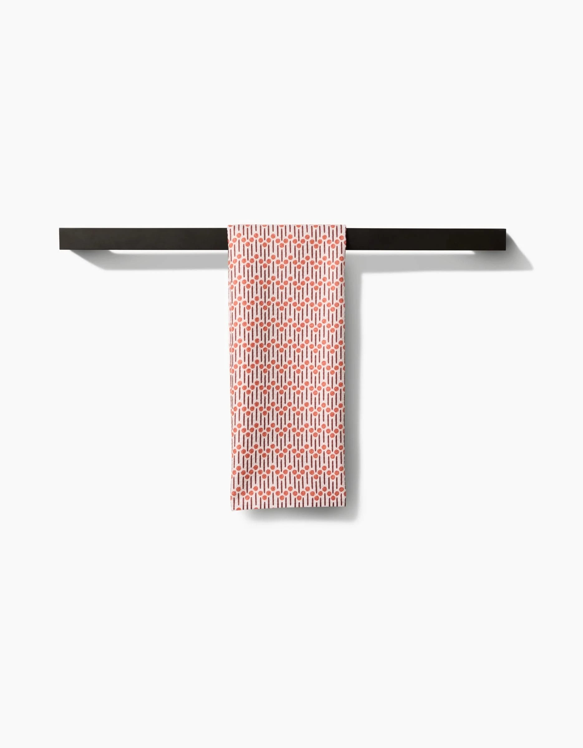 A red and white Retro Geo tea towel by Teri the Butter, made from recycled materials, hangs neatly over a sleek black towel bar on a plain white wall.
