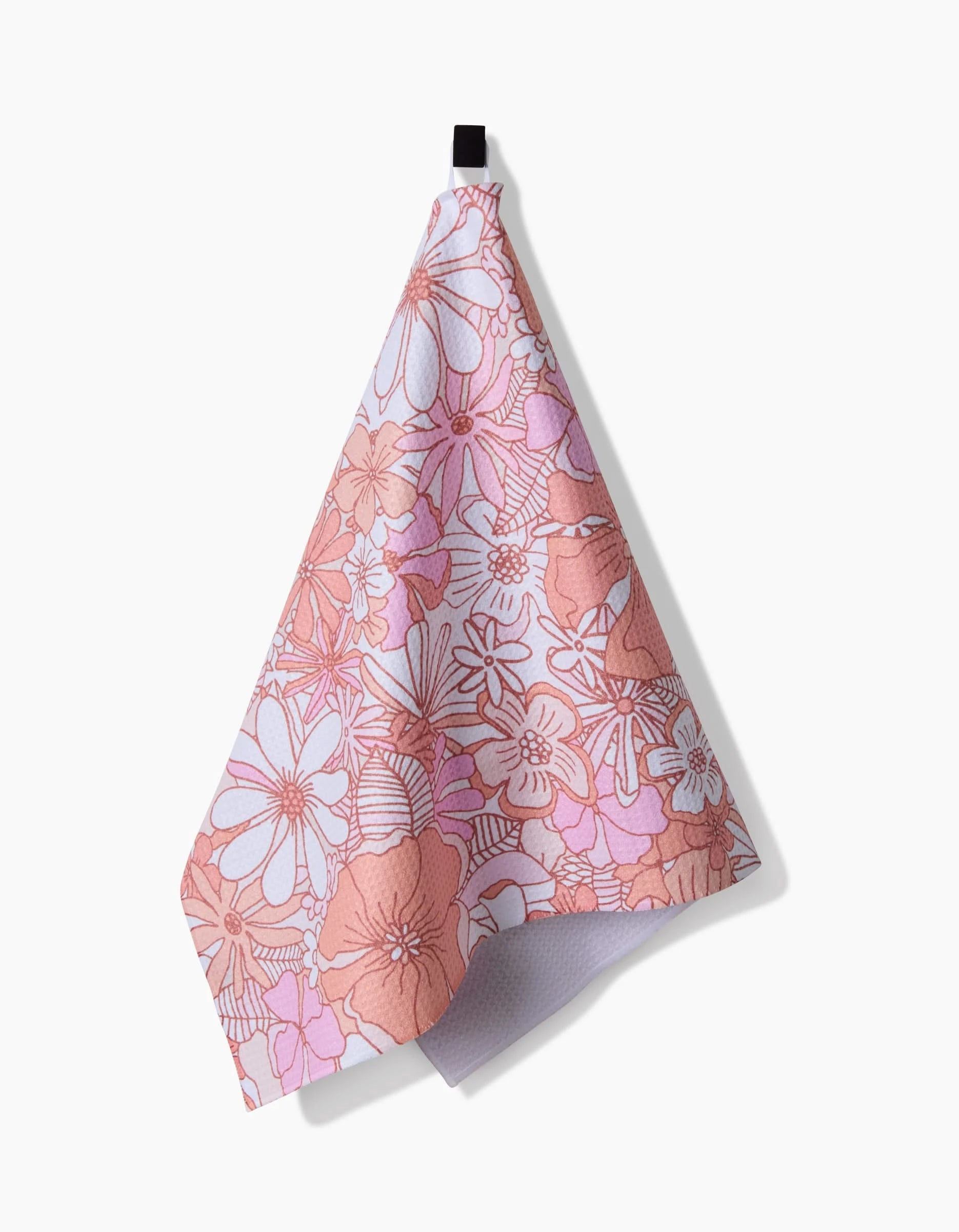 The Retro Vibes Tea Towel by Marina Solodka, featuring a pink and red floral design on recycled materials, hangs from a black loop against a white background with its shadow cast to the right.