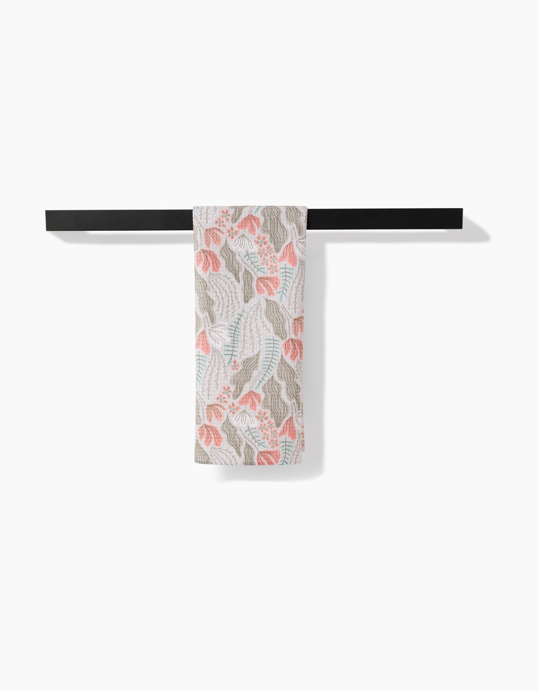 The Amy MacCready Rollie Tea Towel, made from Geoweave fabric with post-consumer recycled materials, features pink, light blue, and beige leaf designs and hangs over a black towel bar against a white background.