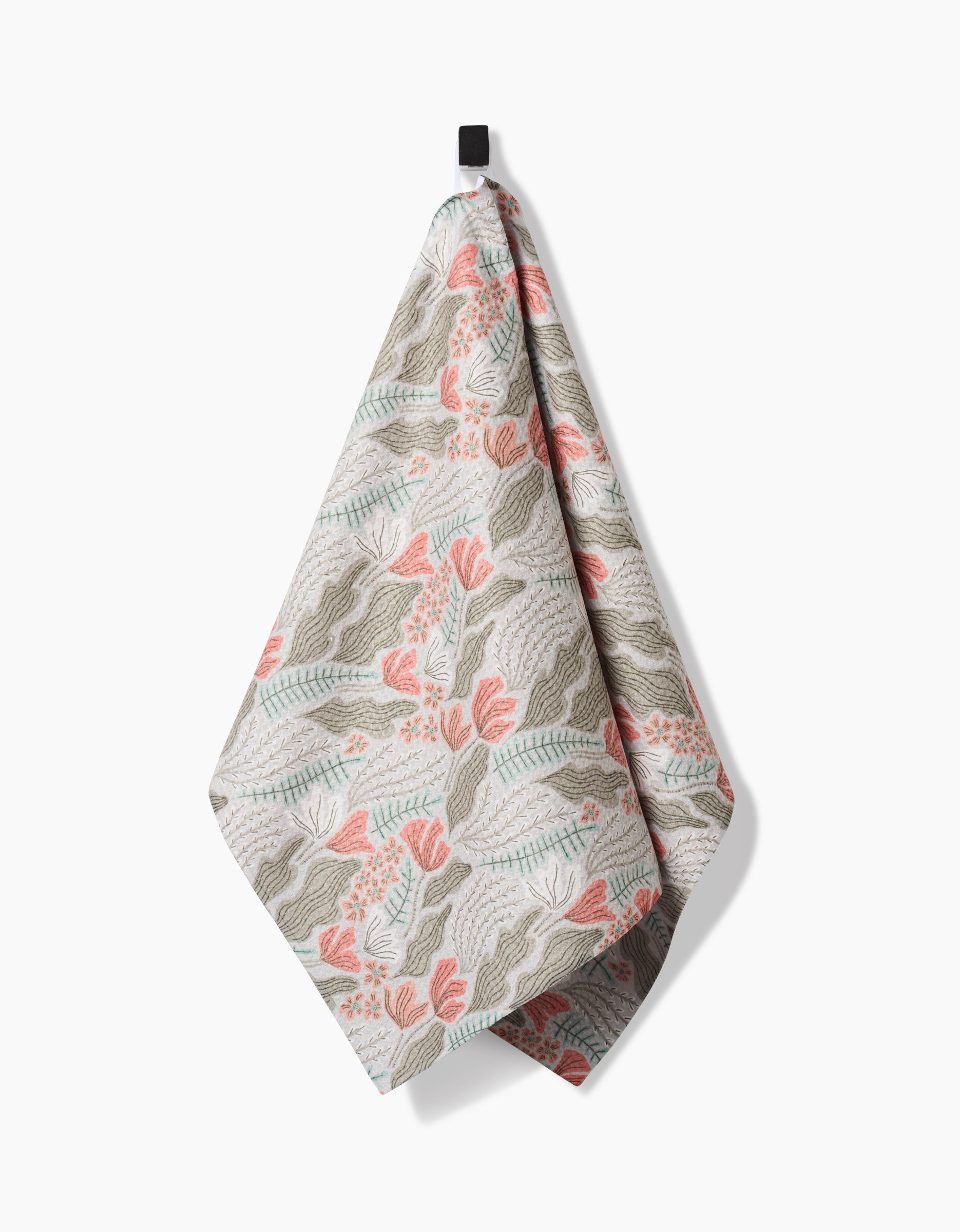 The Amy MacCready Rollie tea towel, featuring a botanical design in muted green, pink, and beige, hangs from a black hook against a white background.