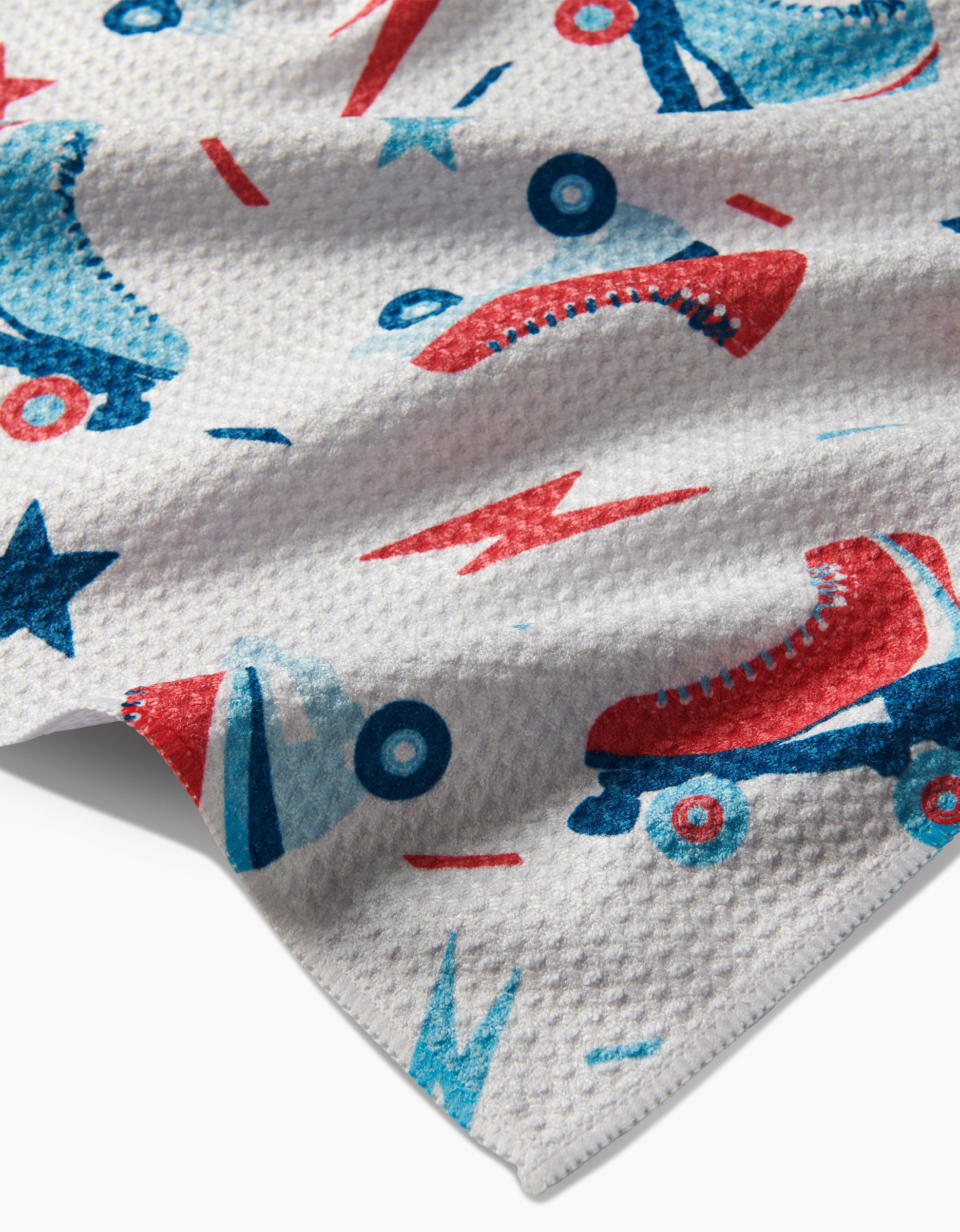 A close-up of Hufton Studio’s Rolling With Stars ultra-absorbent white fabric with a repeating pattern of red and blue roller skates, stars, and lightning bolts.