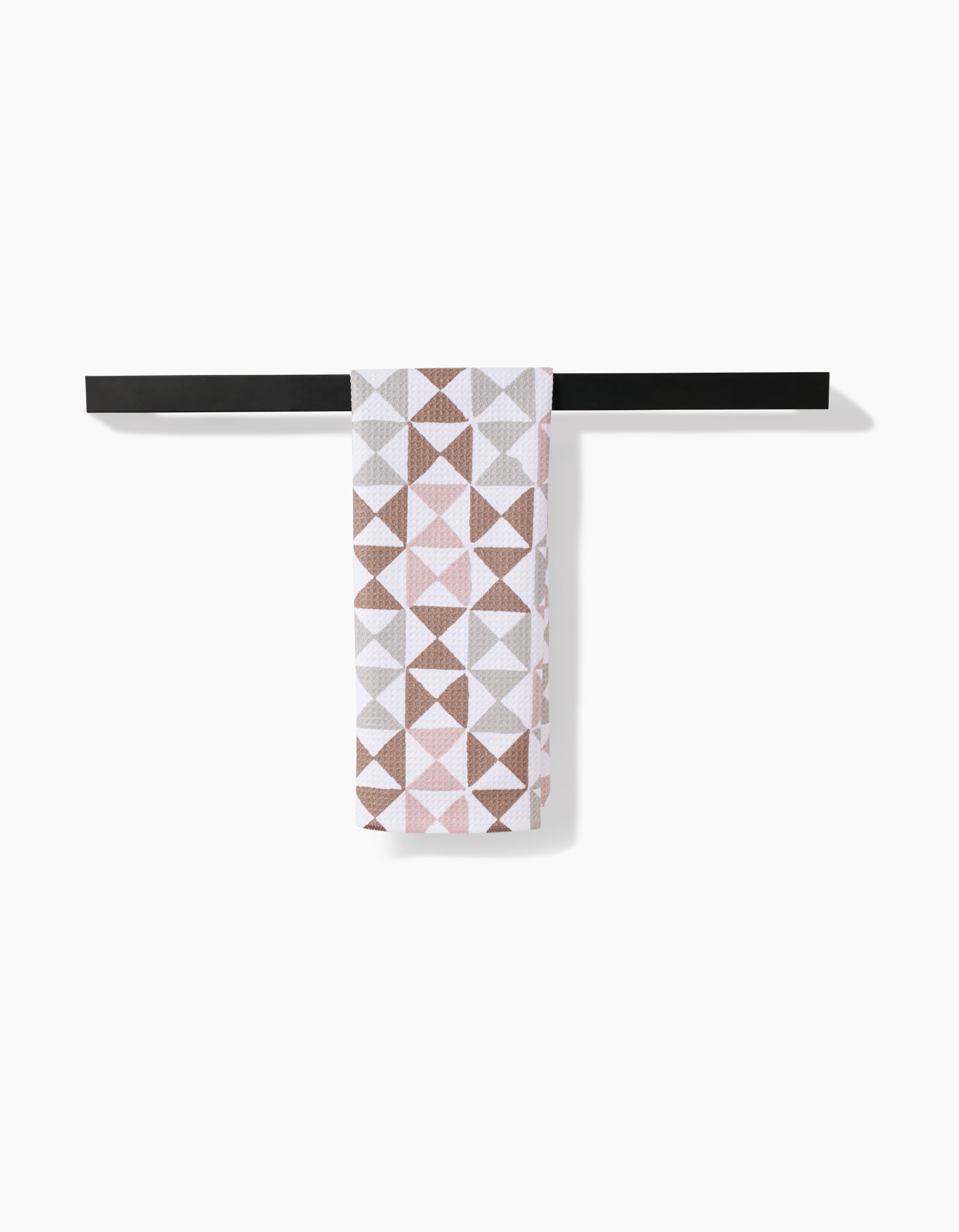 The Rubix tea towel by Studio Jeannot, crafted from recycled materials and decorated with brown, pink, and gray geometric triangles, hangs neatly on a black towel bar against a white background.