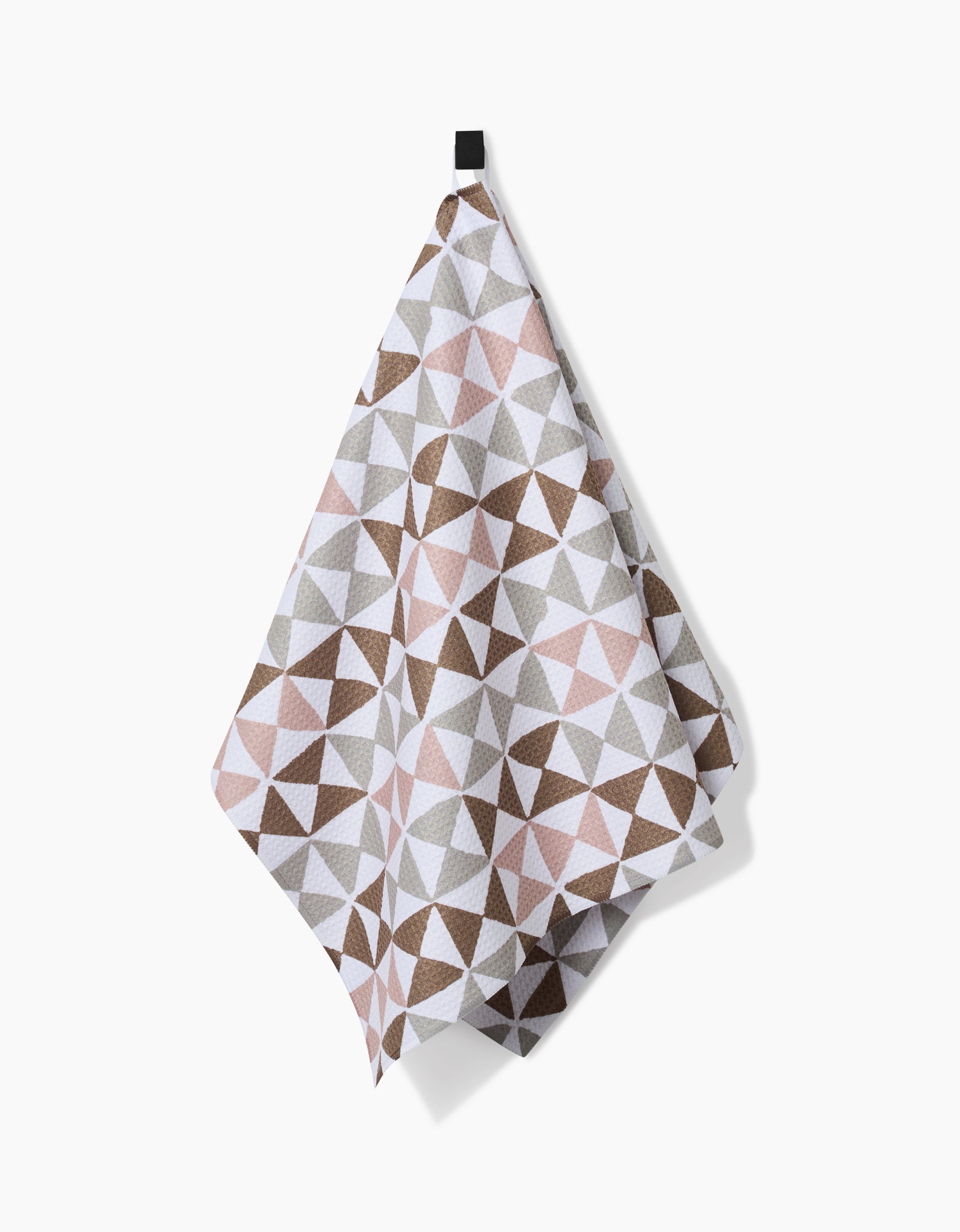 The Rubix tea towel by Studio Jeannot, featuring a geometric triangle pattern in brown, gray, and pink Geoweave fabric, hangs from a black loop against a white background.