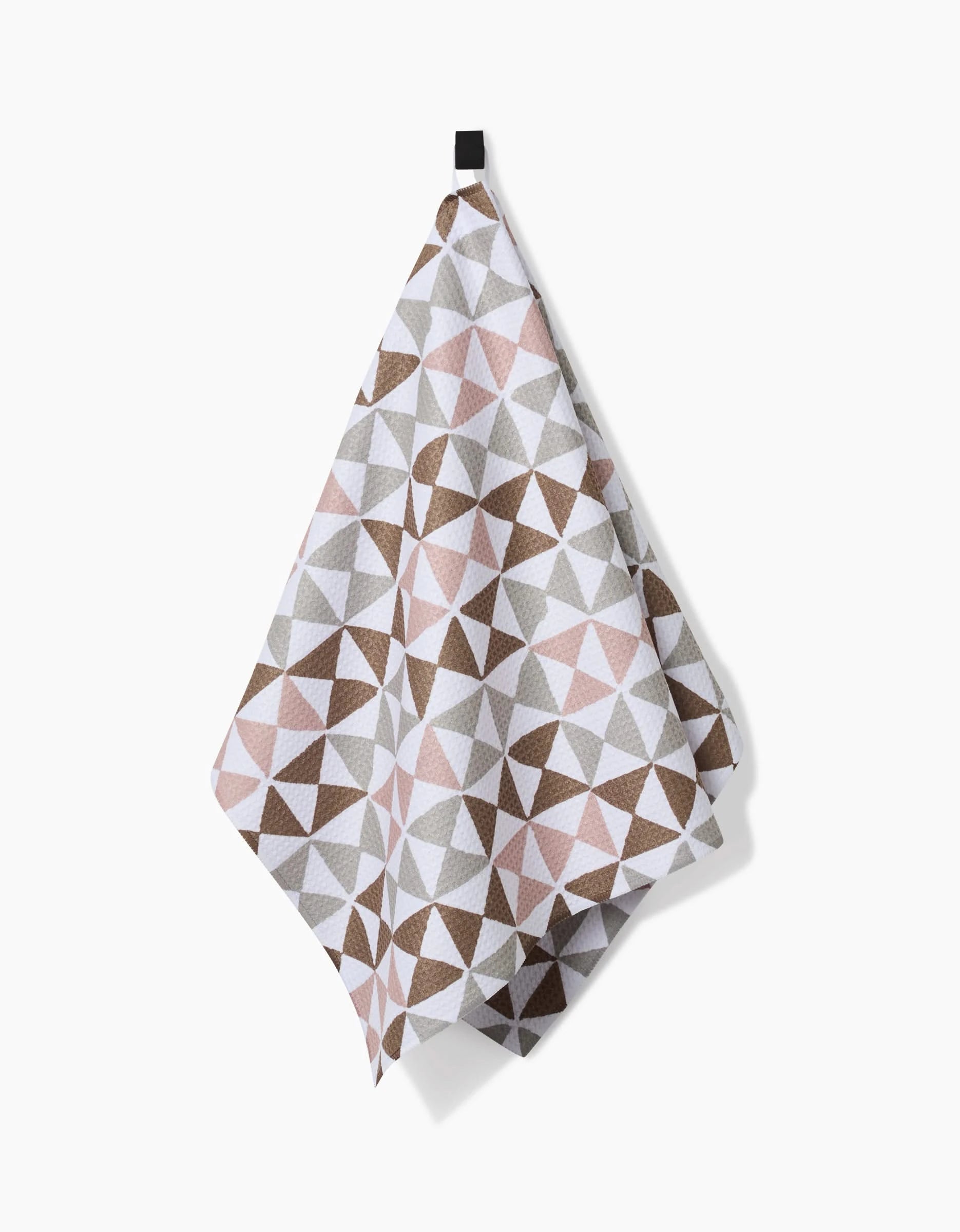 The Rubix tea towel by Studio Jeannot, featuring a geometric triangle pattern in brown, gray, and pink Geoweave fabric, hangs from a black loop against a white background.