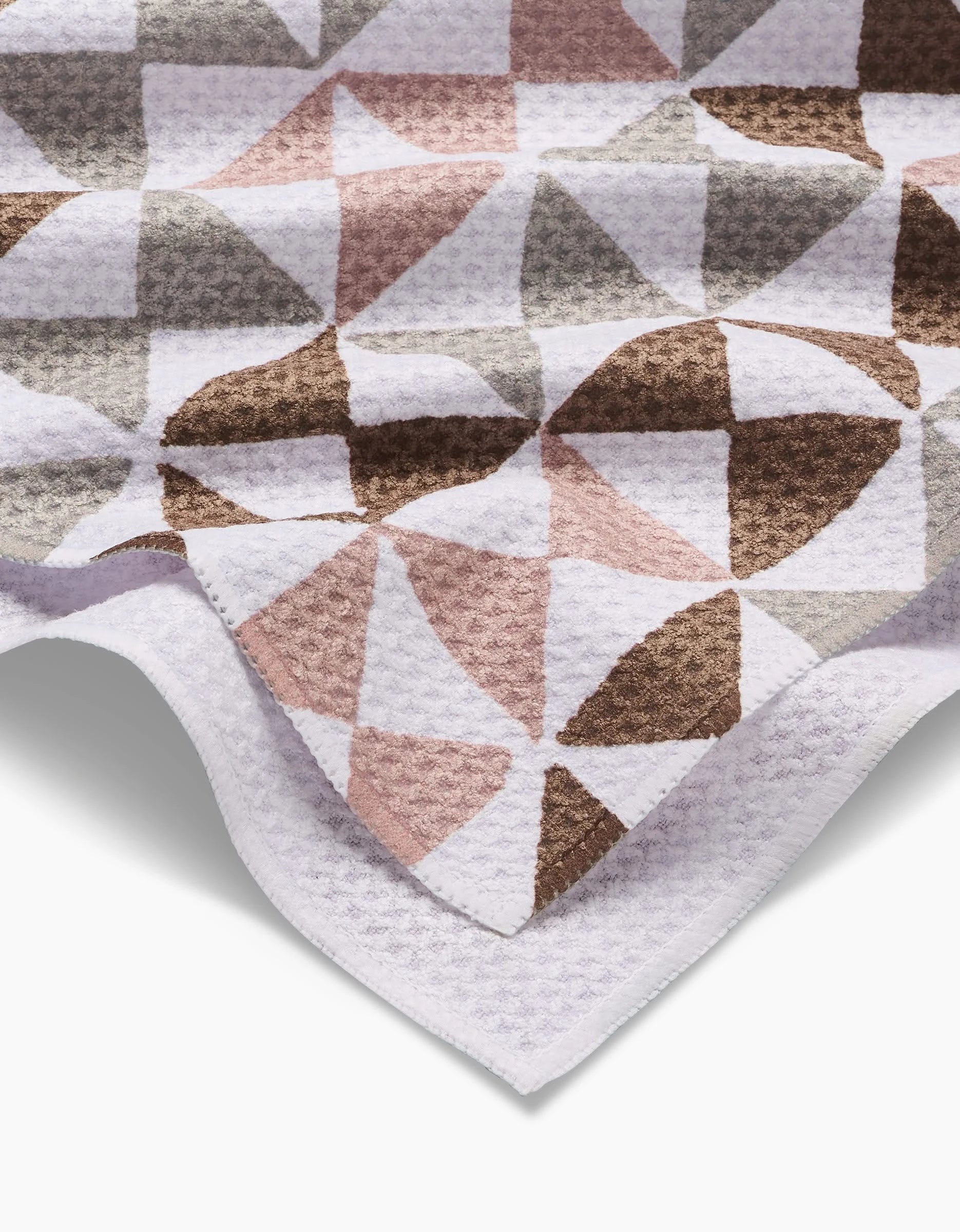 The Rubix tea towel by Studio Jeannot showcases a geometric pattern of overlapping semi-circles in muted brown, pink, gray, and white tones. Made from recycled materials, it features a crisp white border along the edge.