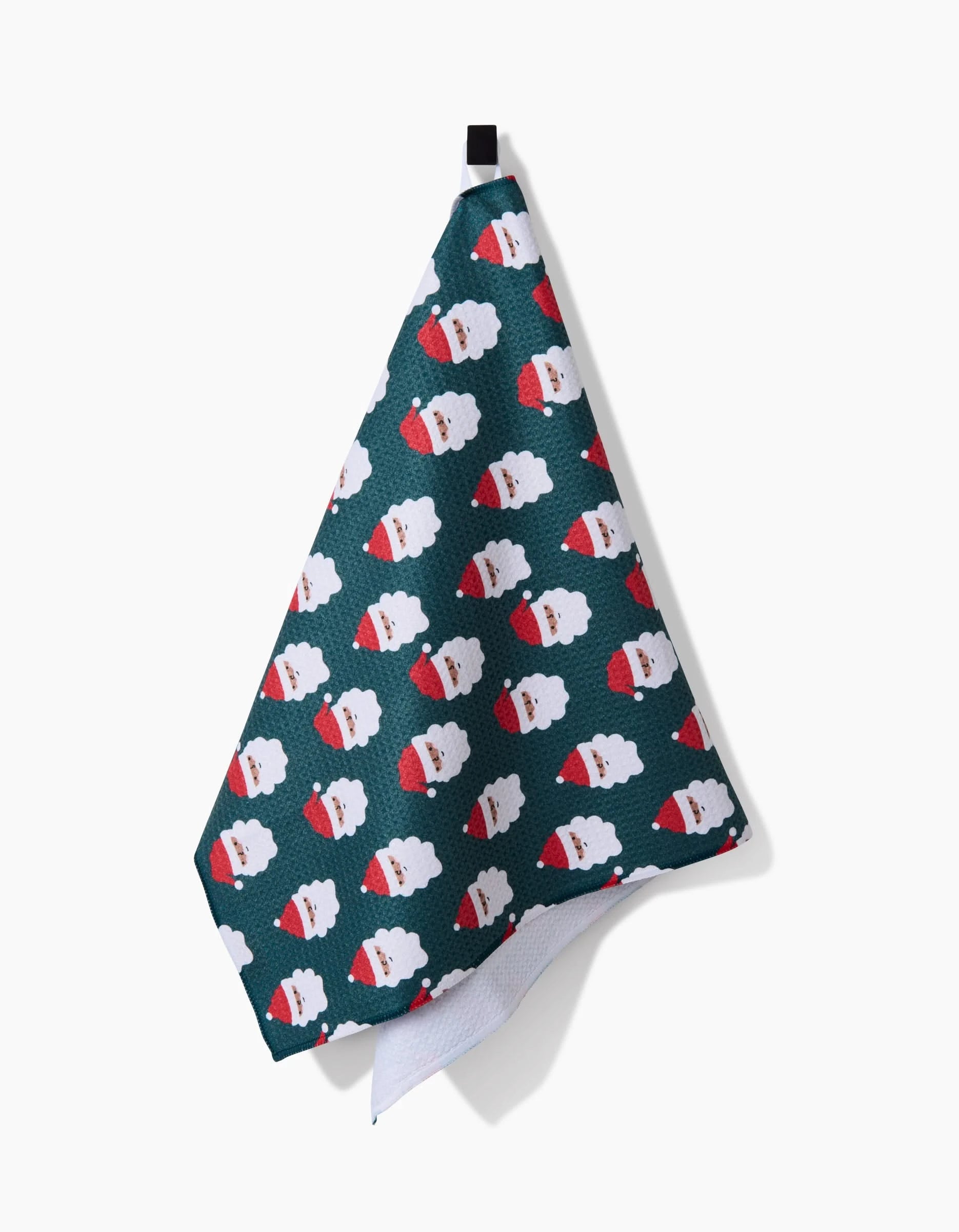 The Santa Santa tea towel by Charlie Rowan Designs features a dark green color, recycled materials, and a repeating Santa Claus face pattern with red hats. It hangs from a black loop and is shown against a white background.