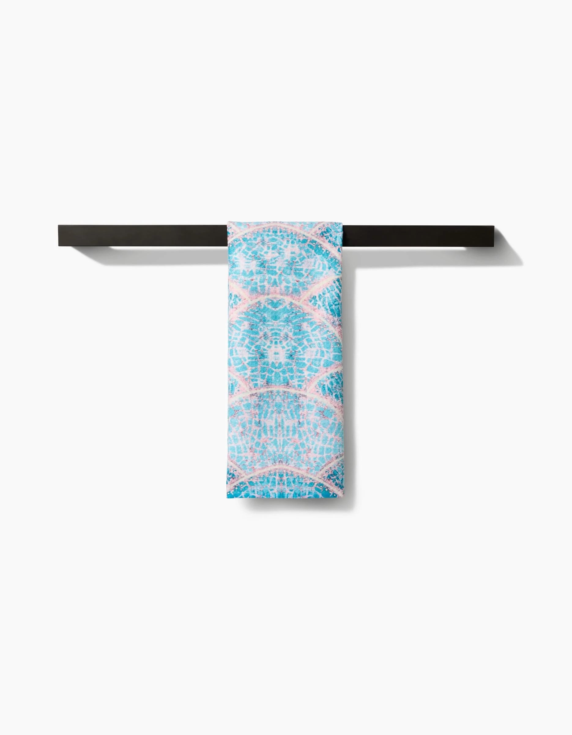 A blue and pink patterned Scallop Hills tea towel by Taryn Brennan, made from recycled materials, hangs neatly on a modern black towel bar with a plain white background.
