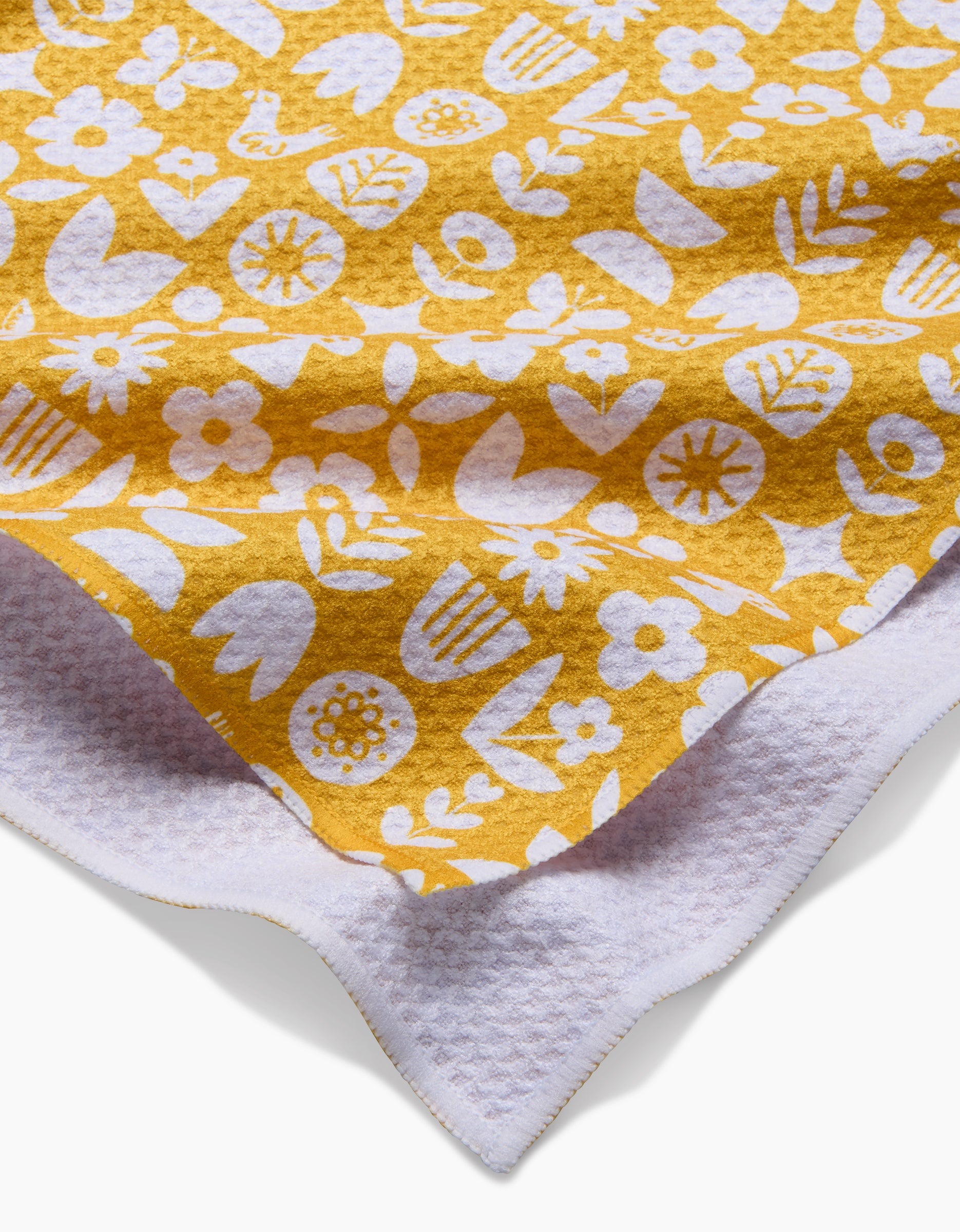 A close-up of the Kayla Ann Scandi Spring yellow blanket, featuring a white floral and leaf pattern, layered over white textured Geoweave fabric for added durability and style.