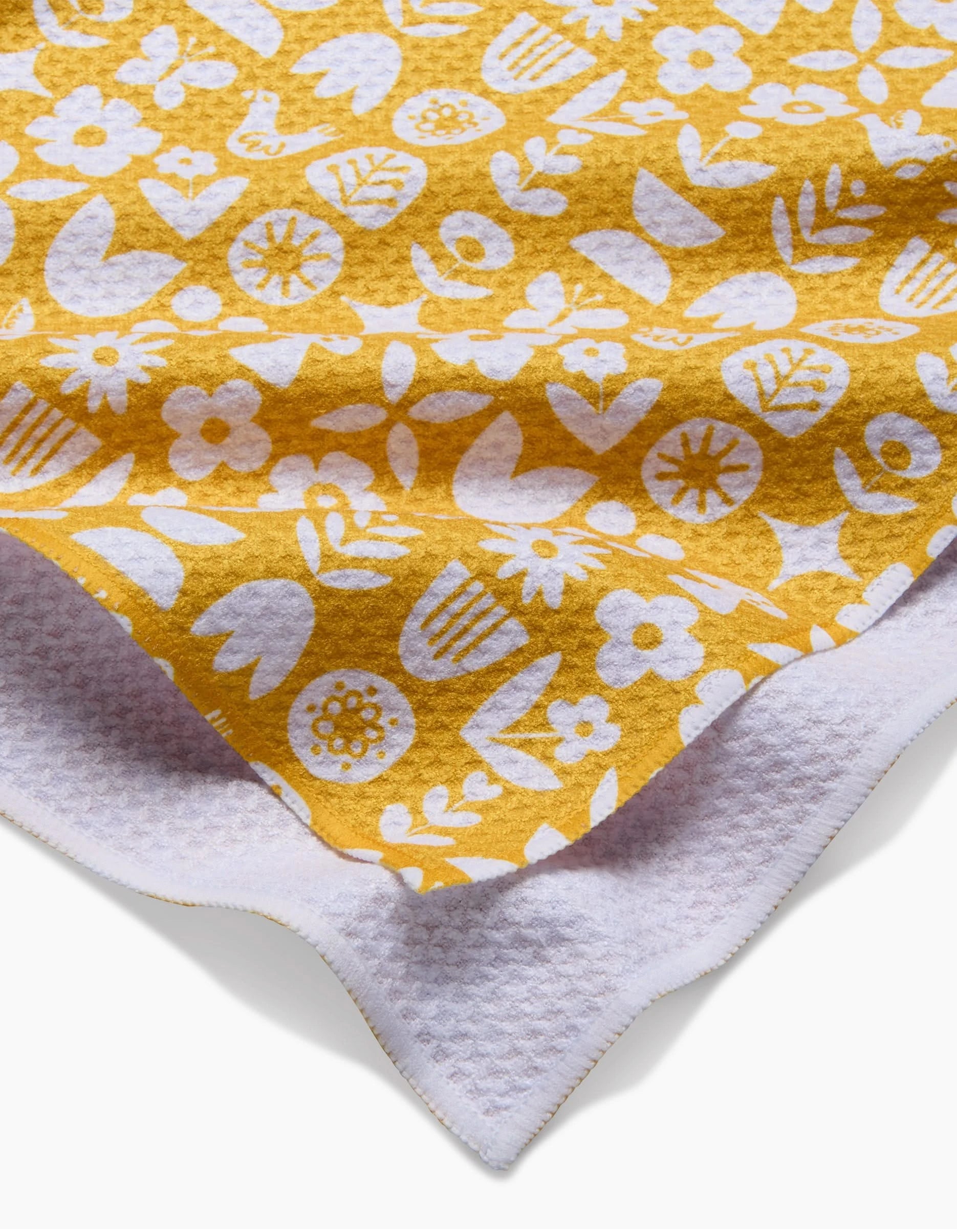 A close-up of the Kayla Ann Scandi Spring yellow blanket, featuring a white floral and leaf pattern, layered over white textured Geoweave fabric for added durability and style.