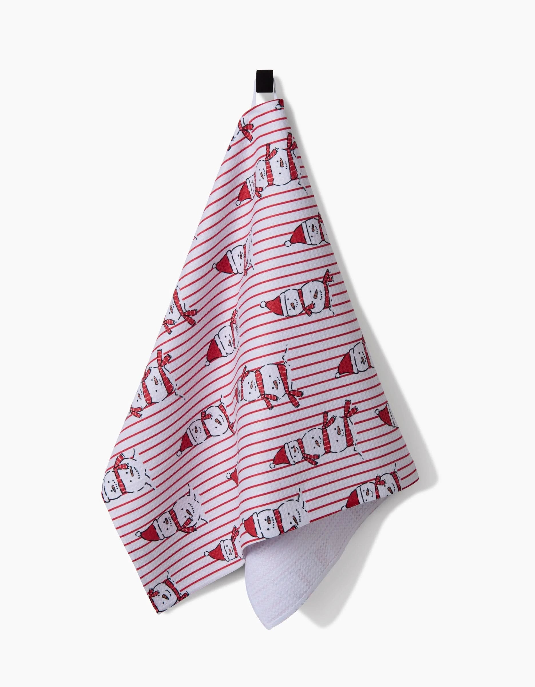 The Hufton Studio Silly Snowman kitchen towel, made from recycled materials, features red stripes and Santa faces in red hats. It hangs on a black hook against a plain white background.