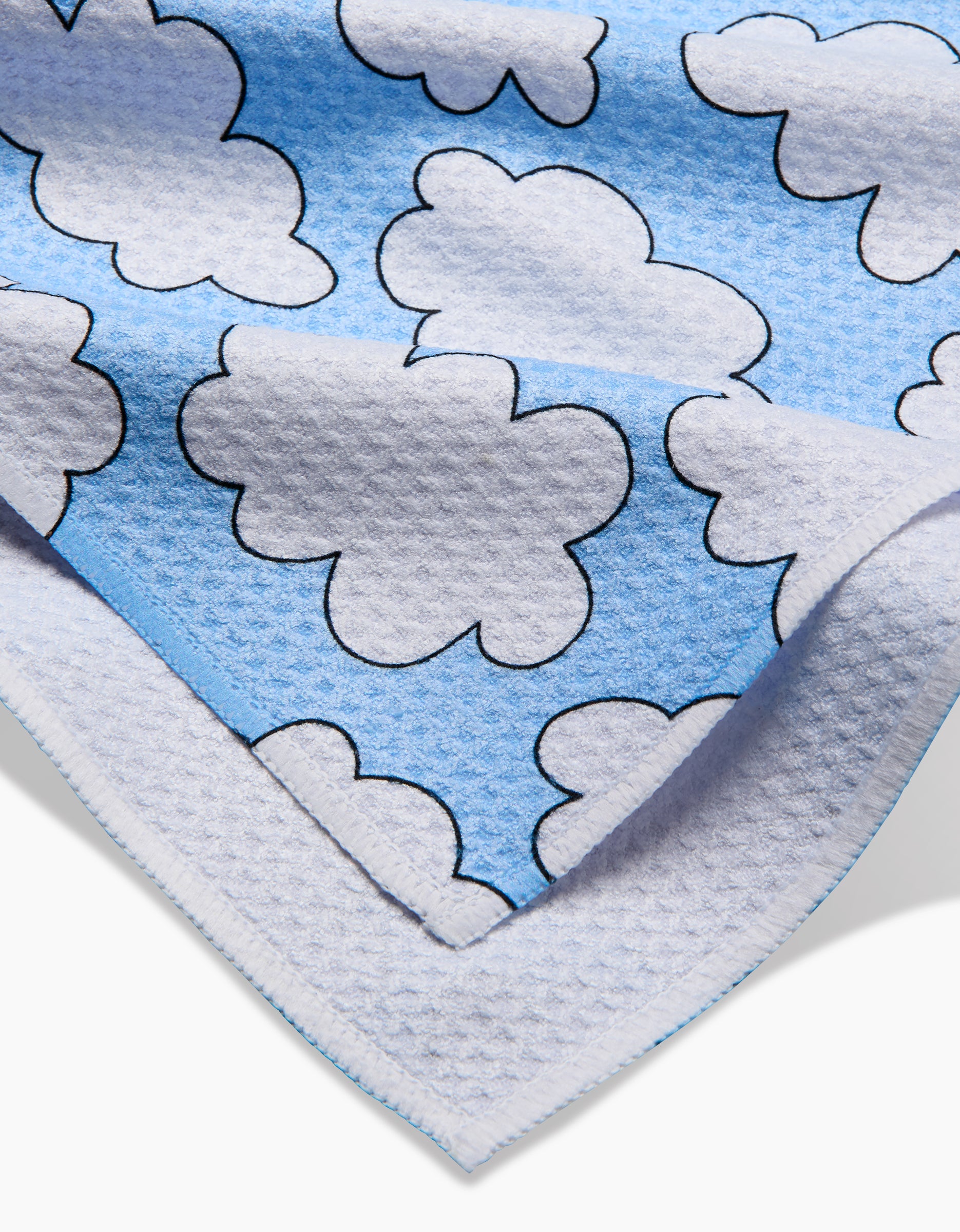 The Mindfulnice Silver Linings blanket is made from eco-friendly Geoweave fabric in soft blue and white, featuring black-outlined cartoon clouds and shown folded at one corner.