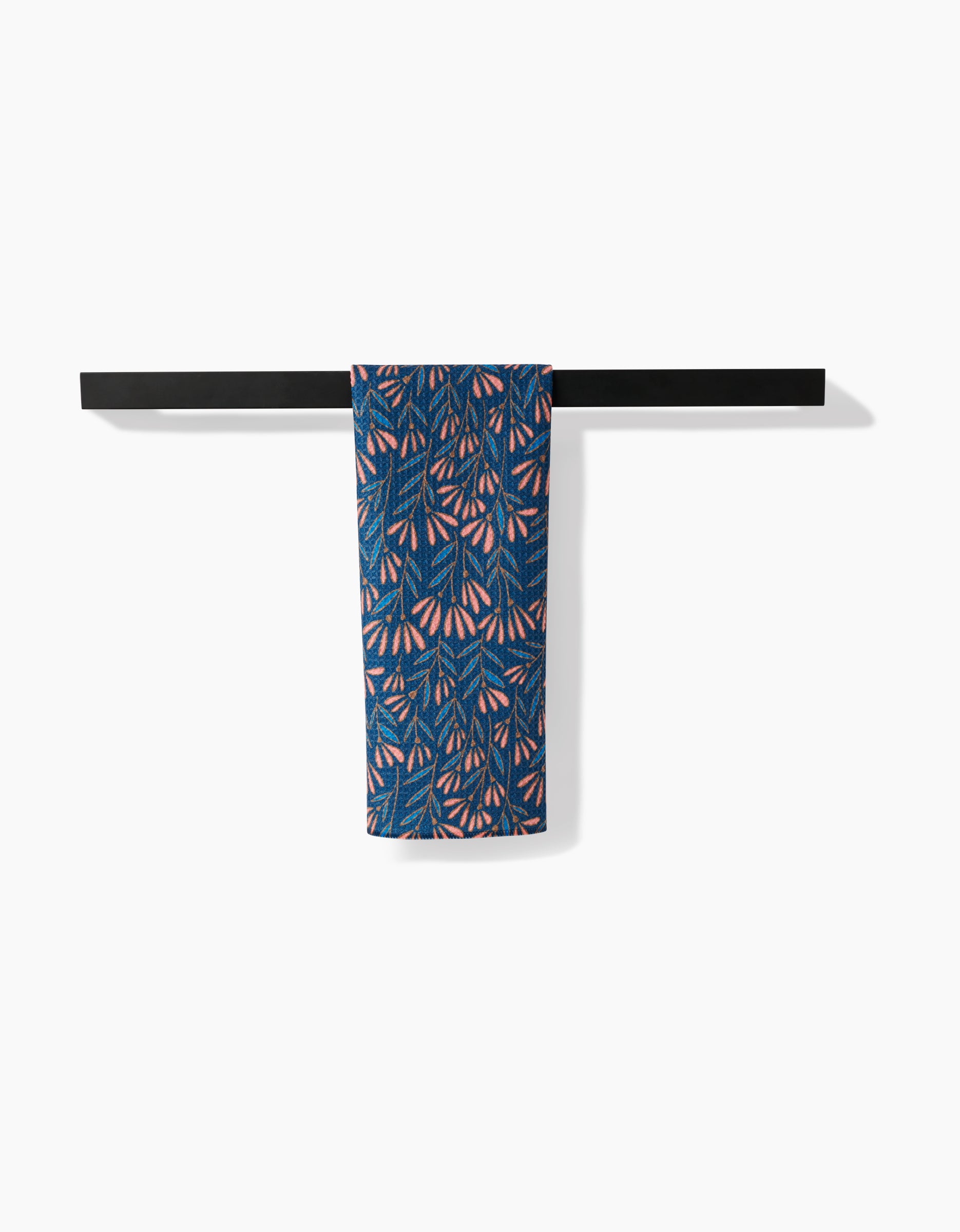 The Amy MacCready Sirocco tea towel, featuring blue, pink, and orange leaf patterns, hangs neatly over a black towel bar against a plain white background.