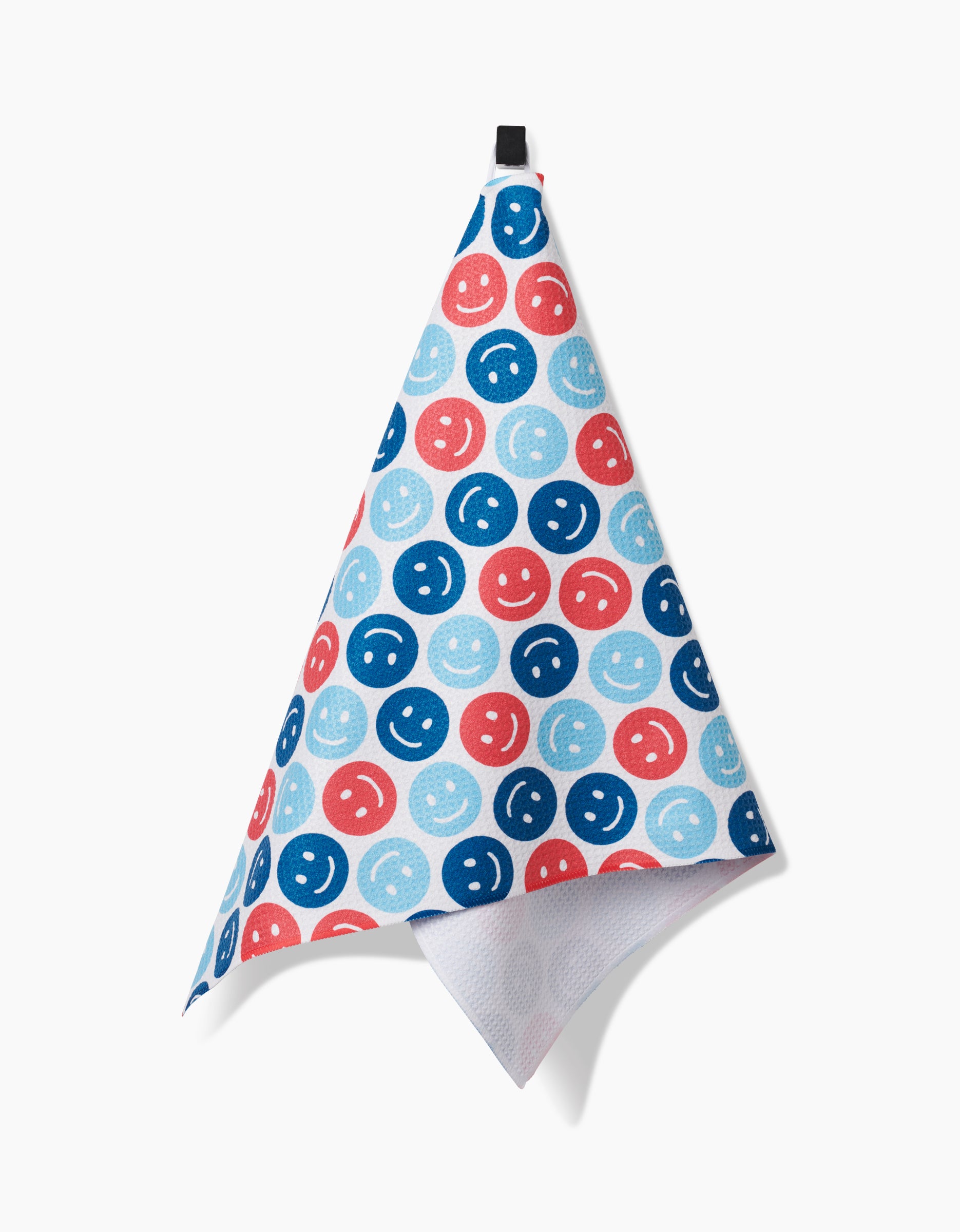 The Smiley Face July tea towel by Hufton Studio is made from recycled materials and showcases blue, light blue, and red smiley faces, hanging from a black loop against a white background.