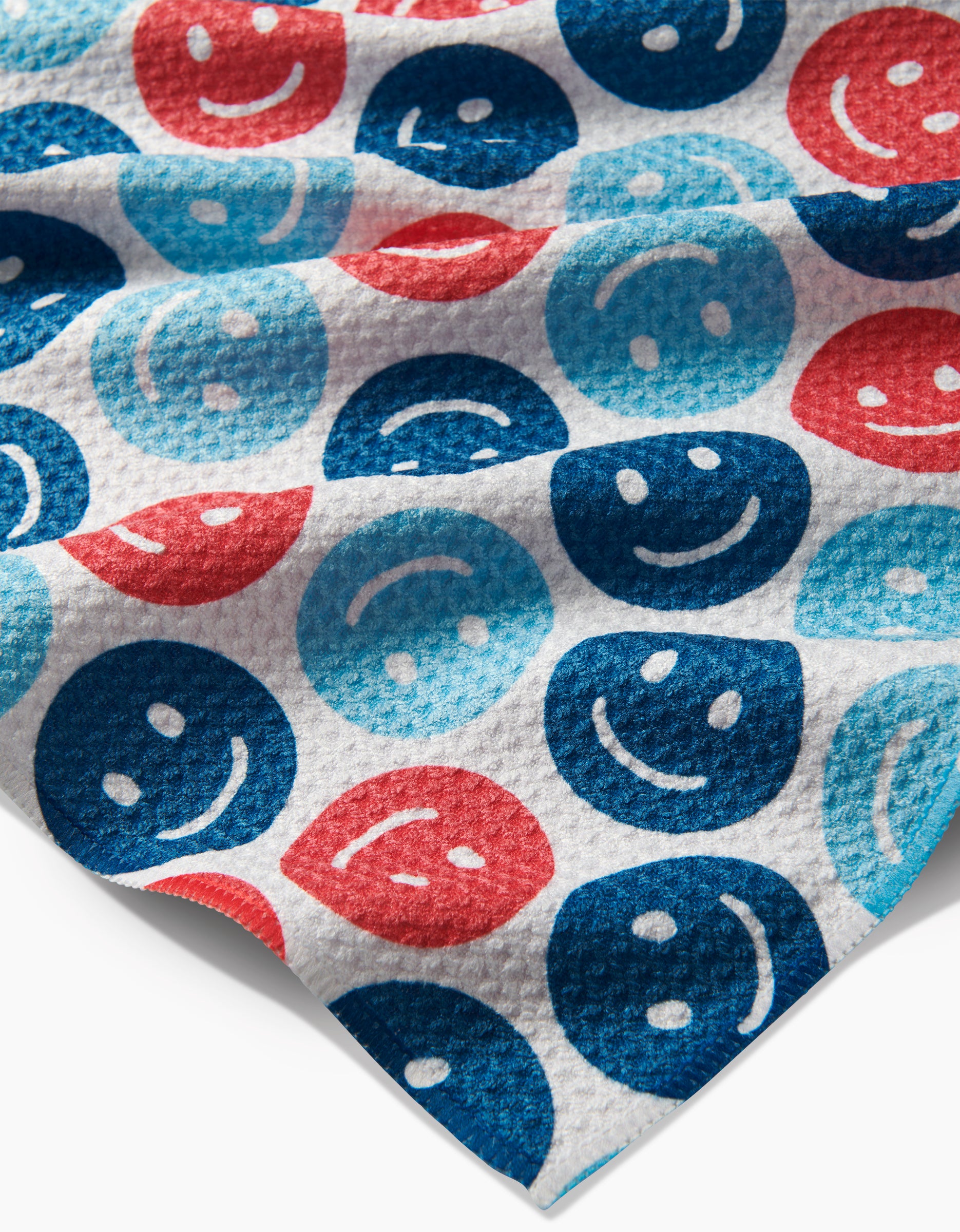 The Hufton Studio Smiley Face July tea towel features a Geoweave fabric patterned with blue, red, and navy smiley and sad face icons in alternating rows. The slightly wrinkled design adds texture to the playful arrangement.