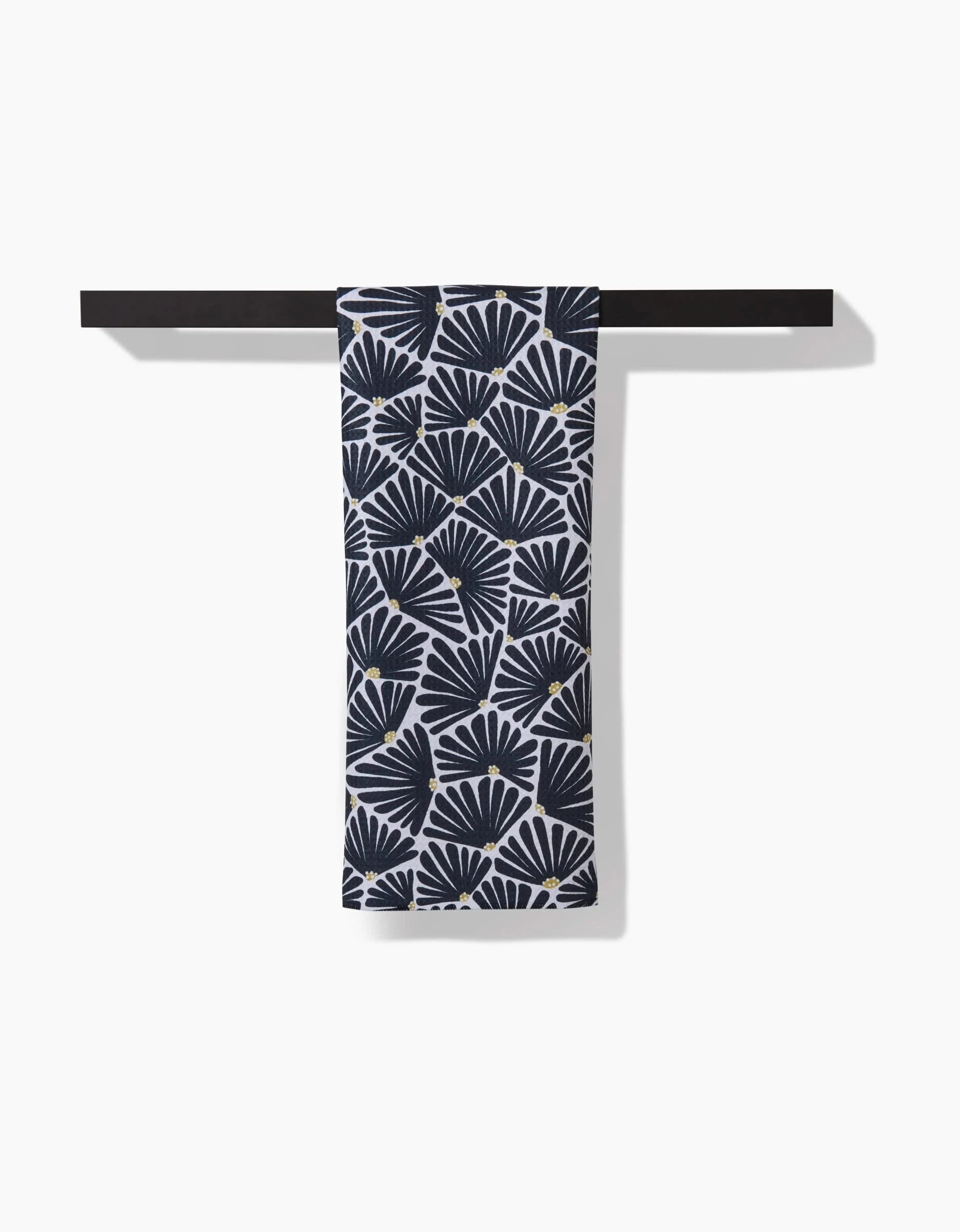 The Solie Black tea towel by Amy MacCready, featuring a repeating dark blue and white fan pattern on ultra-absorbent Geoweave™ fabric, hangs neatly over a black rod against a crisp white background.